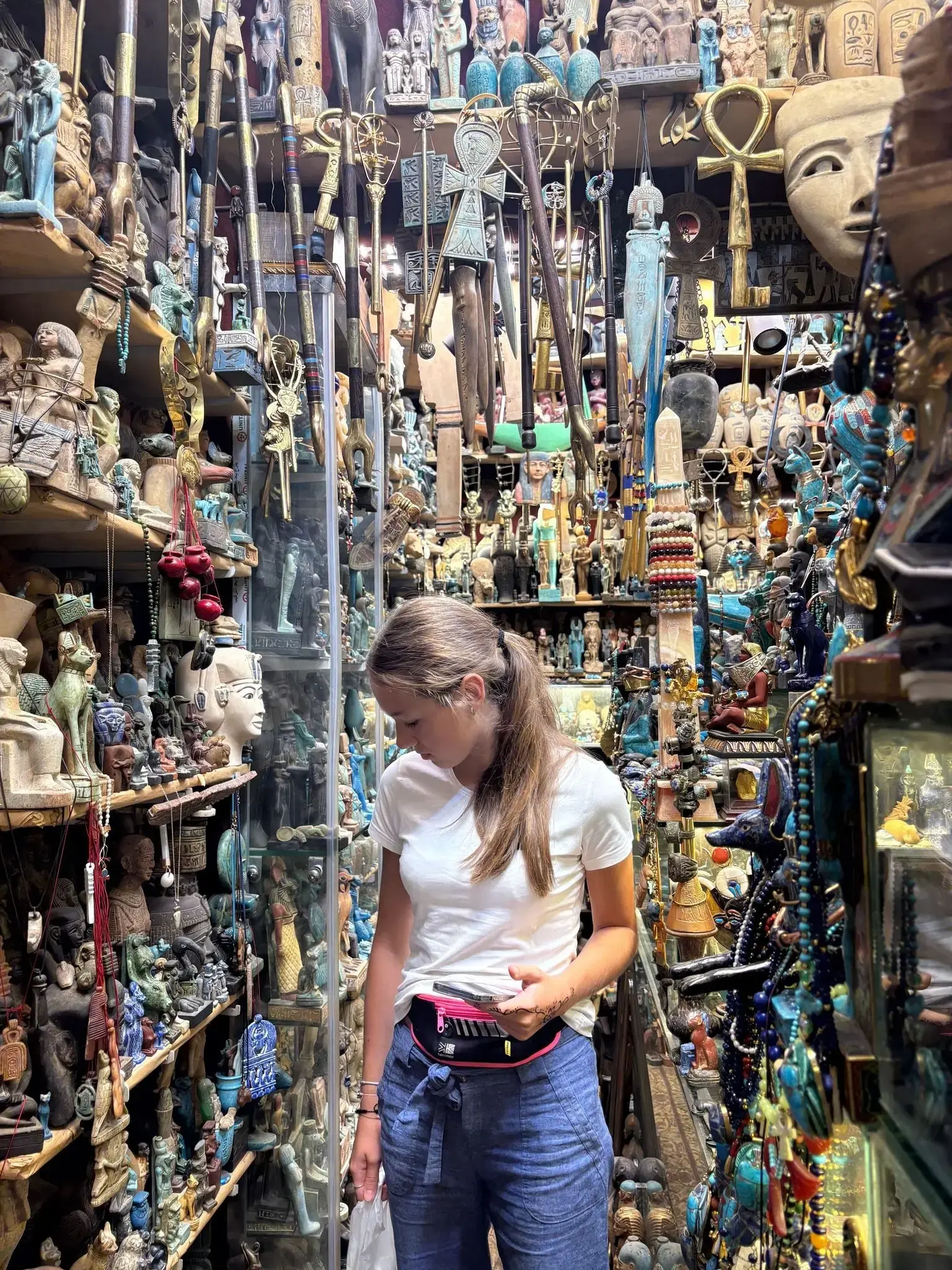 Display of Egyptian artifacts and souvenirs in a Khan el-Khalili shop, Cairo, Egypt, with a traveler browsing nearby during a trip.