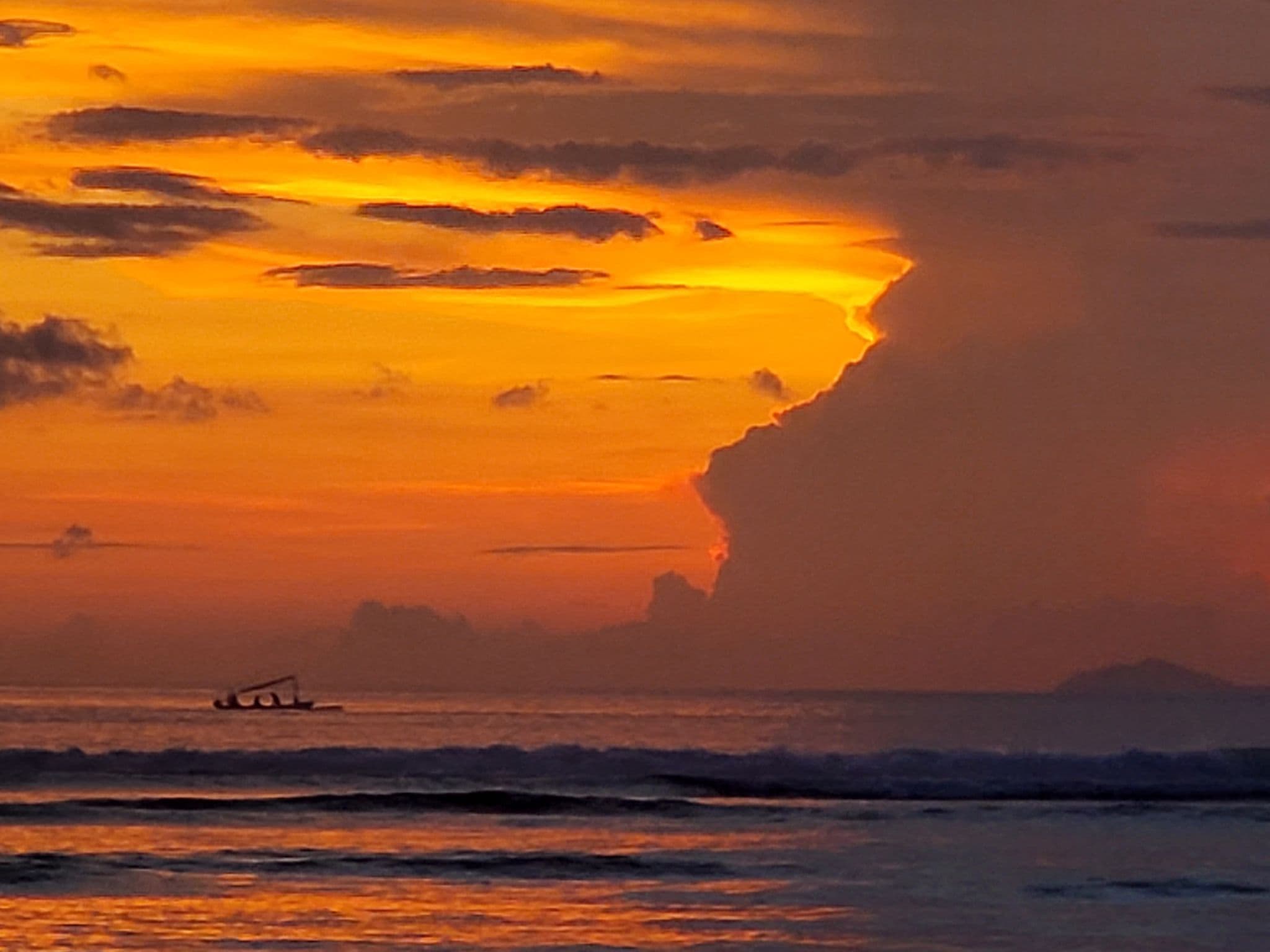 Sunset over the sea at Gili Trawangan, Indonesia, with a silhouetted boat on the water and dramatic glowing clouds.