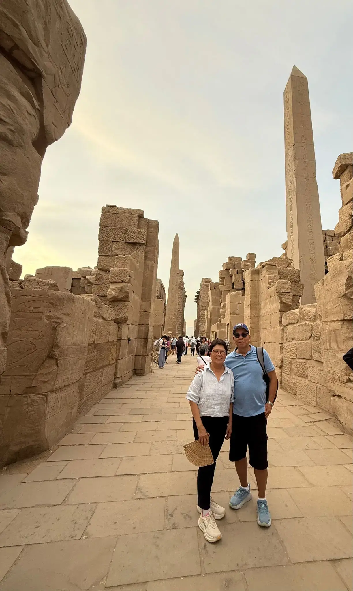Karnak Temple obelisks and ruins with two travelers posing on the walkway in Luxor, Egypt.