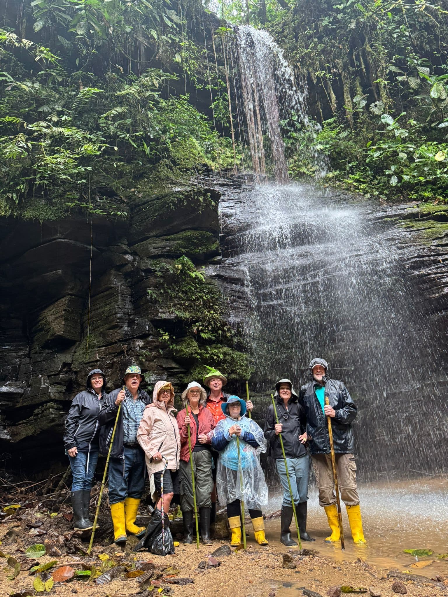 Waterfall in the Amazon rainforest with a group of hikers in rain gear and yellow boots standing at the pool.