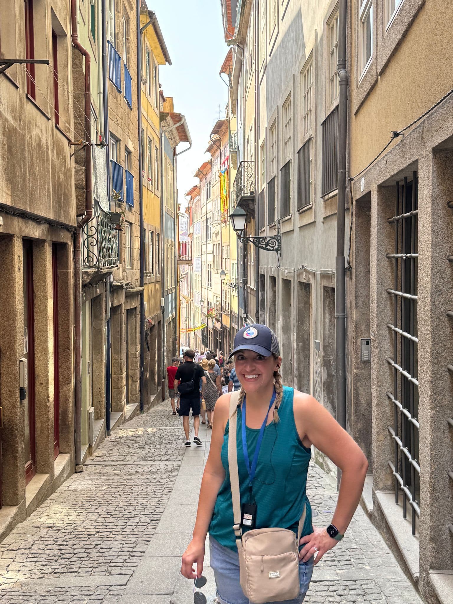Narrow cobblestone street in Porto, Portugal, with a woman posing in the foreground and pedestrians walking behind.