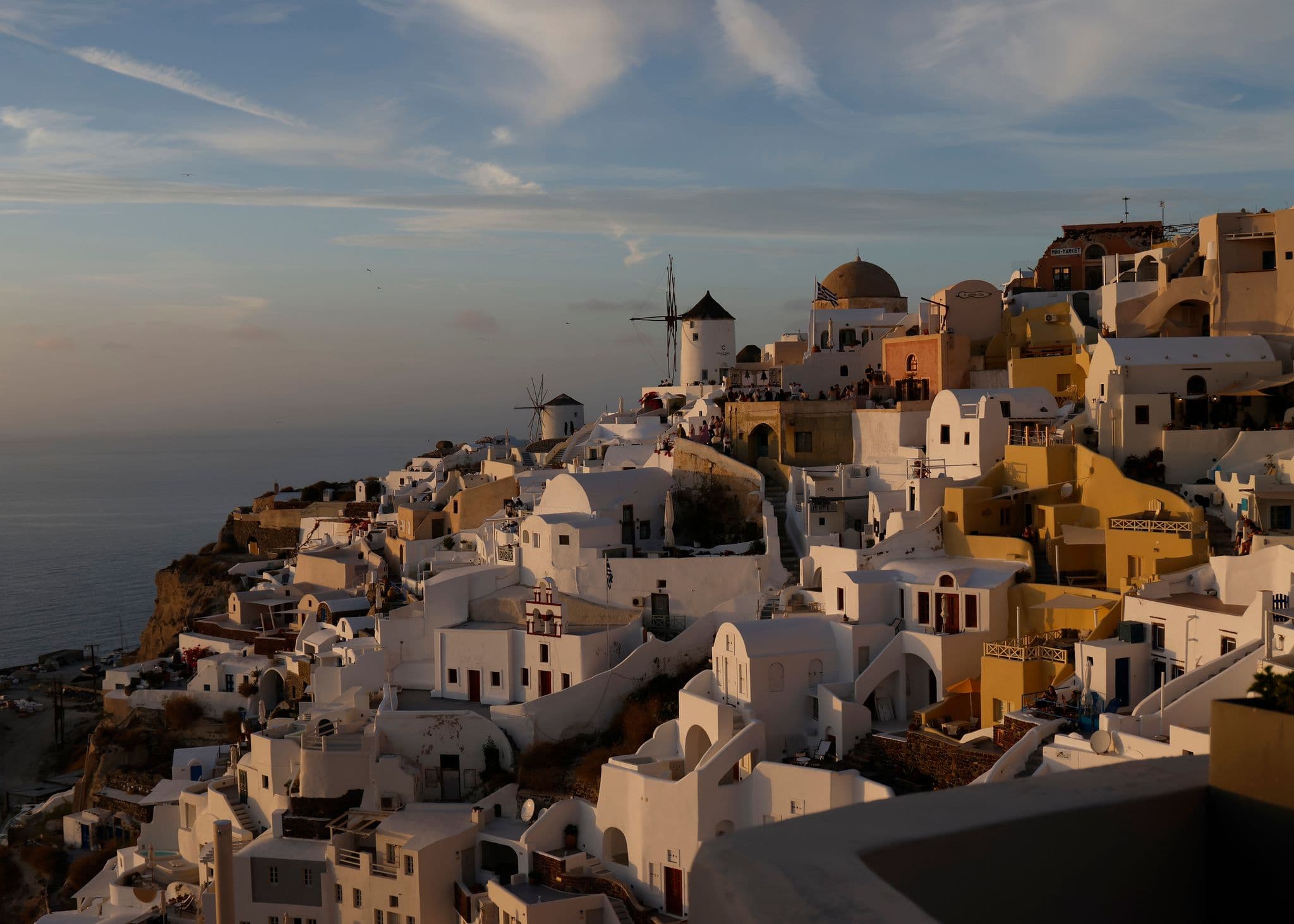 Oia cliffside village in Santorini with whitewashed houses and windmills glowing in sunset over the Aegean Sea, Greece.