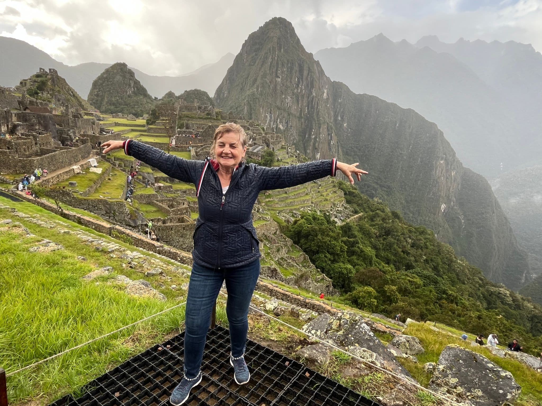 Machu Picchu ruins with a woman standing arms outstretched on a grassy terrace, Cusco region, Peru.