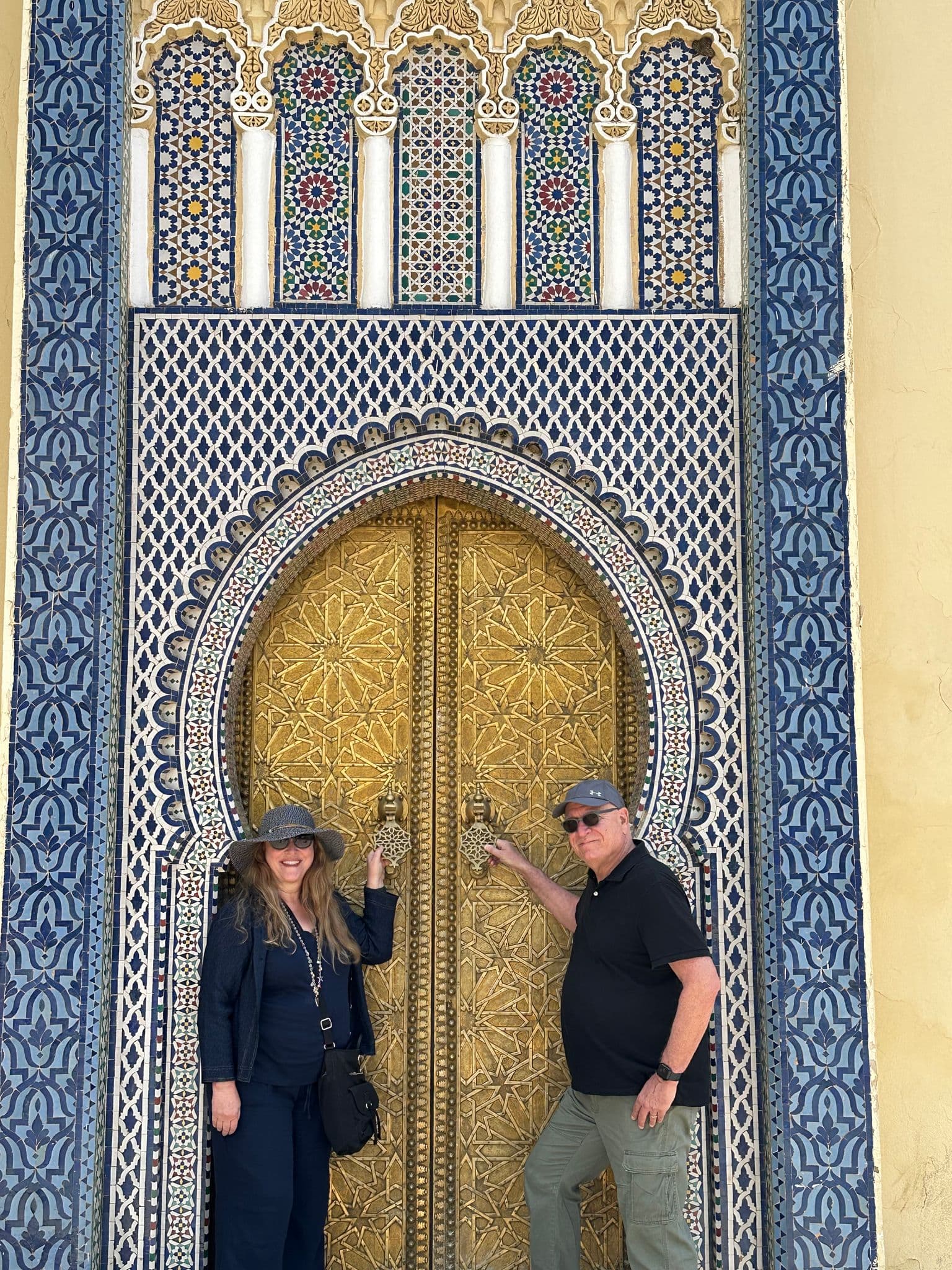 Golden ornate door with two travelers touching the door knockers at an ornamental gate in the Fes medina, Morocco.