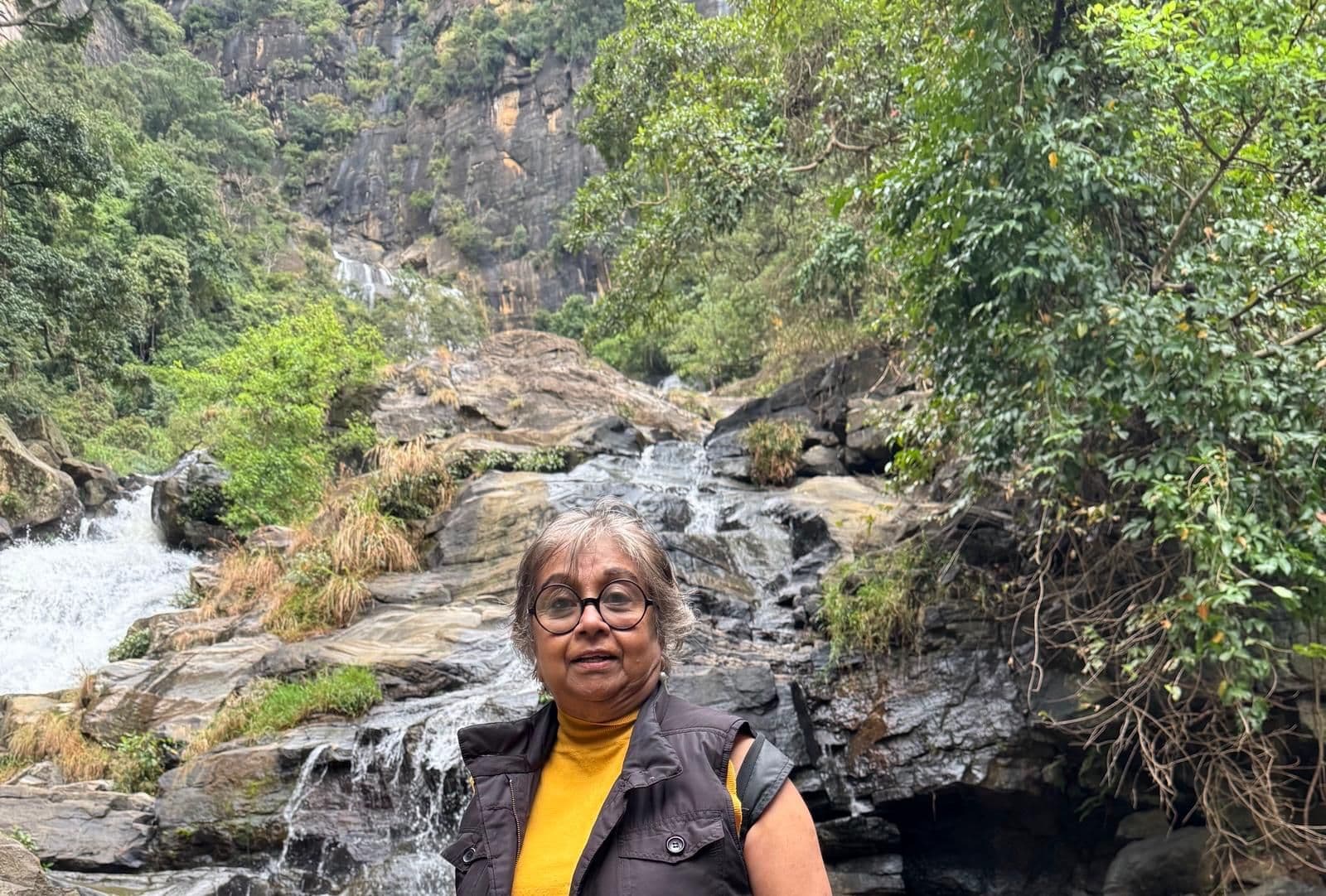 Waterfall cascading over rocky ledges with a traveler standing on rocks in the foreground during a trip.