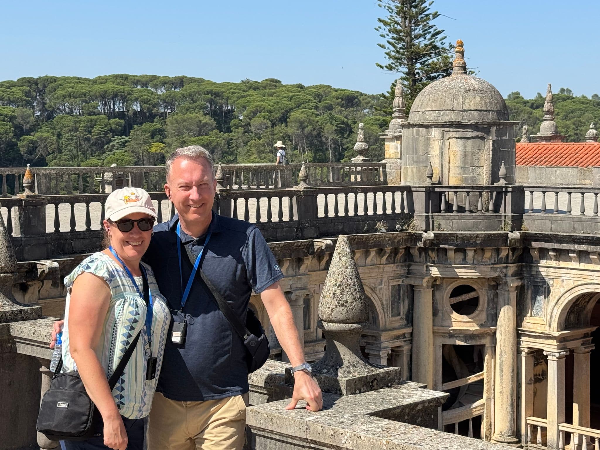 Convent of Christ rooftop terrace in Tomar, Portugal, with a couple posing by a stone balustrade overlooking historic cloisters.
