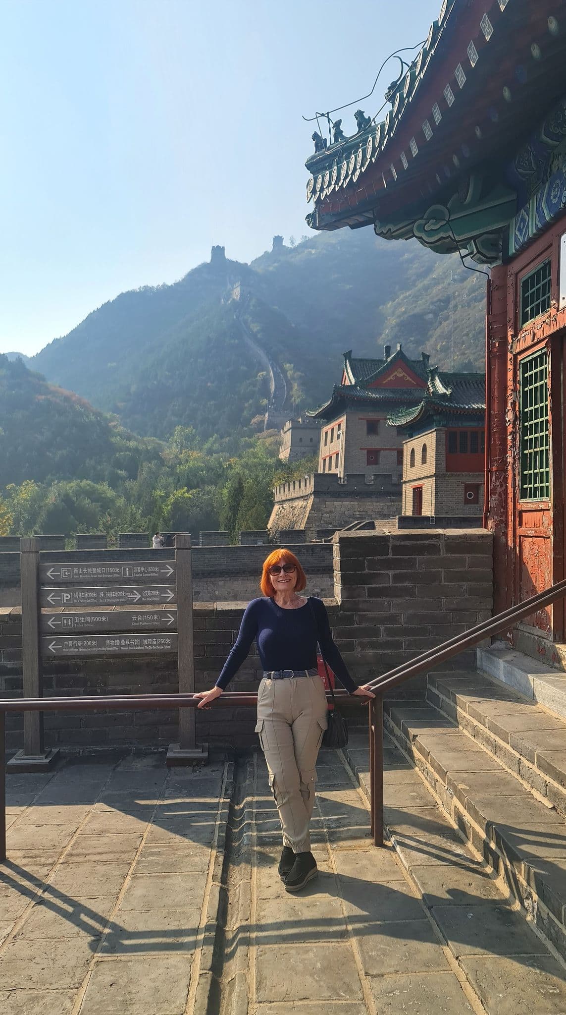 Great Wall of China with a traveler leaning on a railing, posing on a stone terrace with the wall and mountains behind, China