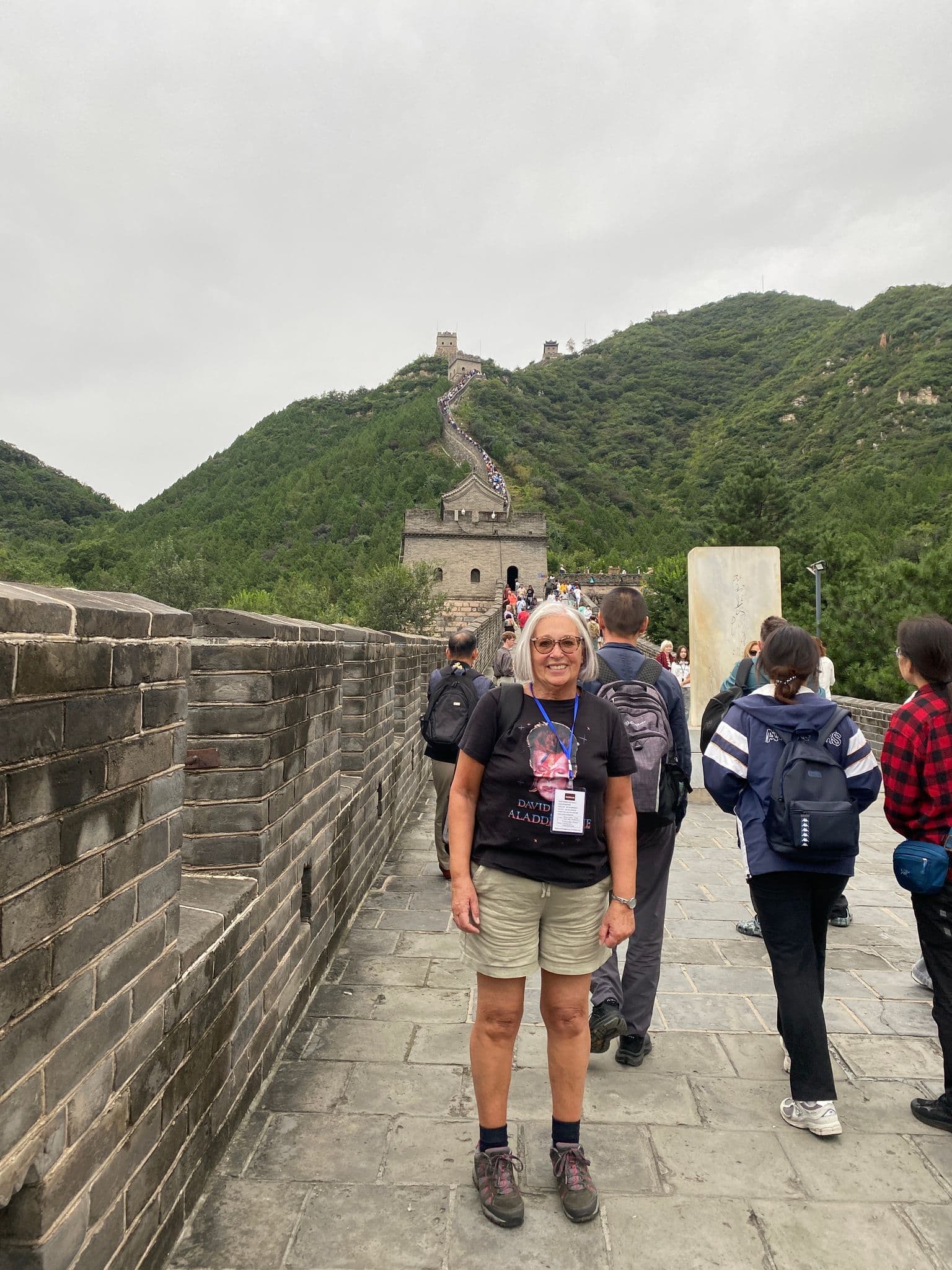 Great Wall of China winding up green hills with a woman tourist standing on the wall, China.