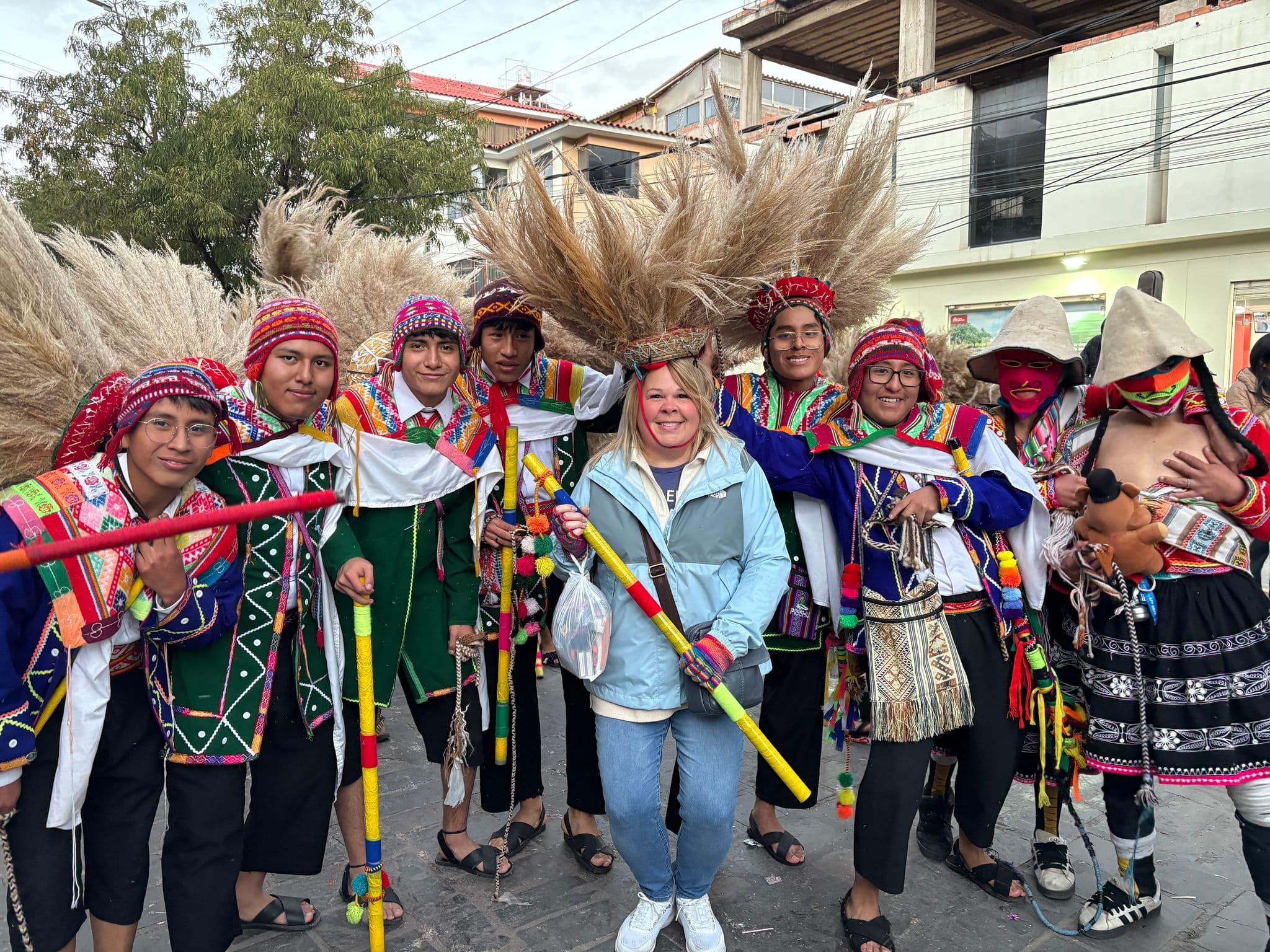 A traveler stands among costumed Andean dancers holding decorated staffs during a street parade in Cusco, Peru.