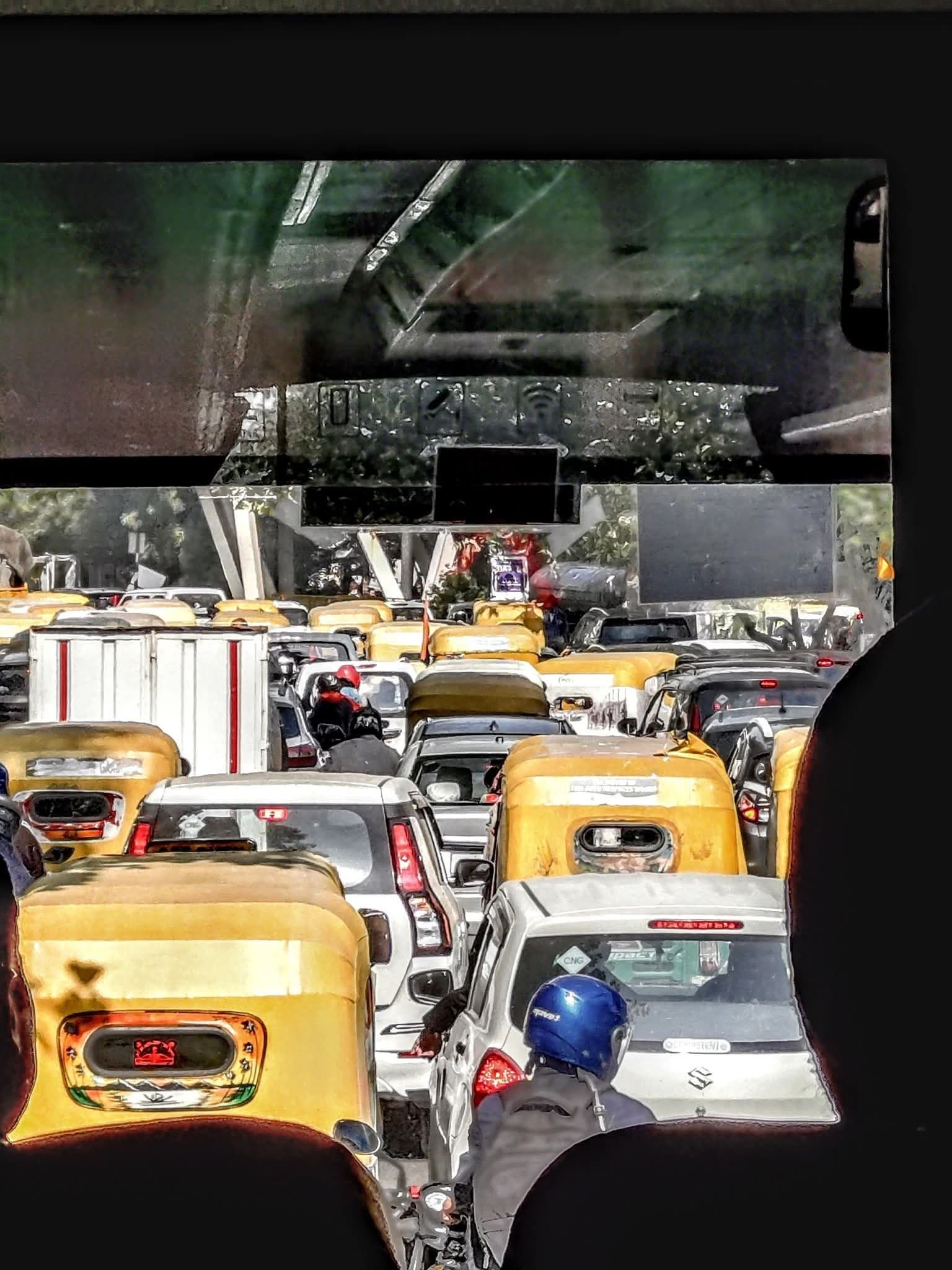 Yellow auto-rickshaws and cars through a minibus windscreen in heavy Delhi traffic with a motorcyclist in a blue helmet, Delhi, India.