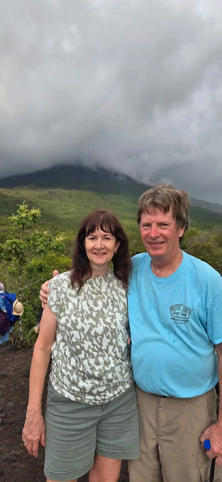 Arenal Volcano shrouded in clouds with a smiling couple posing on volcanic slopes in La Fortuna, Costa Rica.