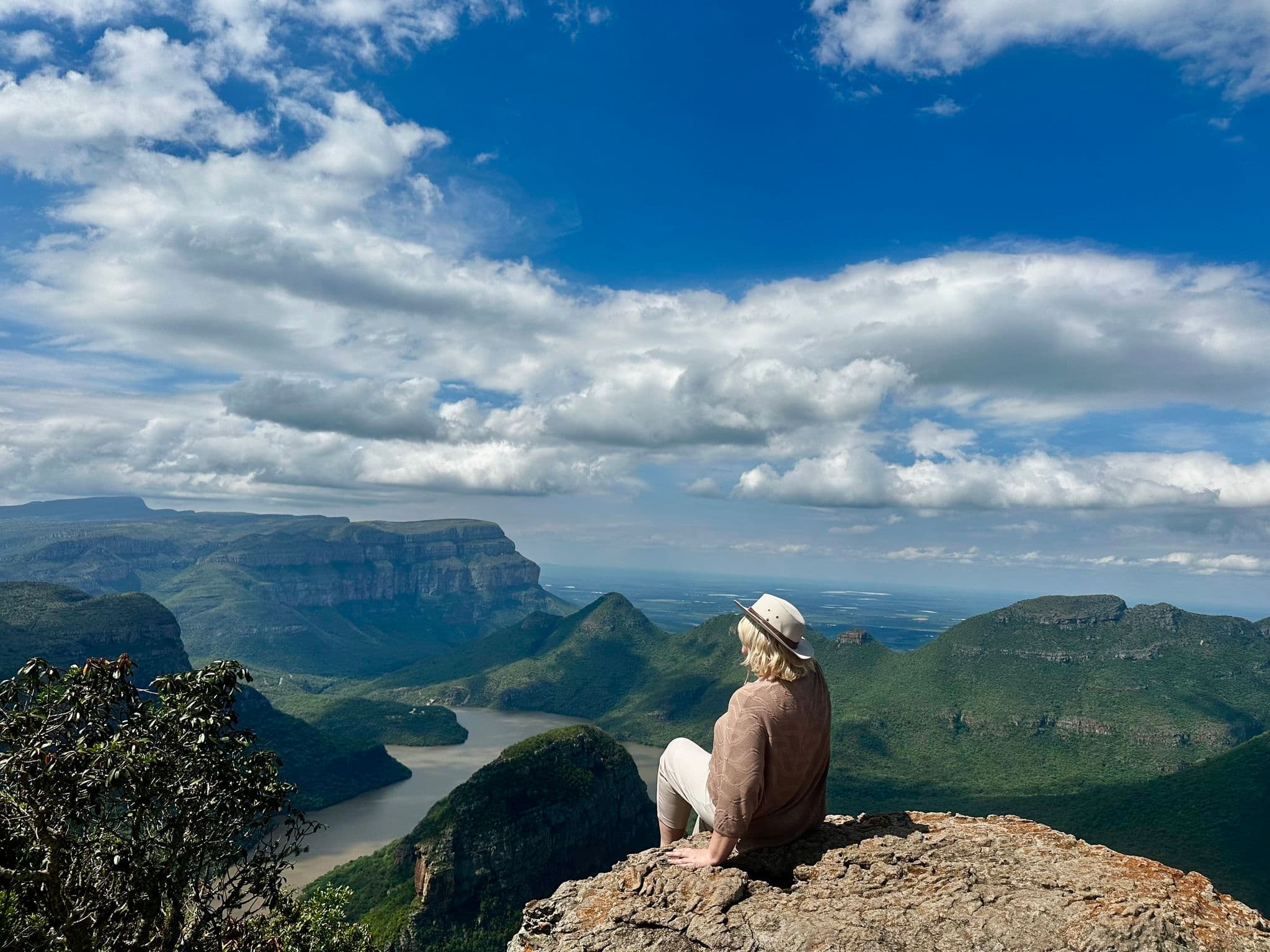 Blyde River Canyon view with a person sitting on a cliff edge overlooking a winding river and green mountains, Mpumalanga, South Africa