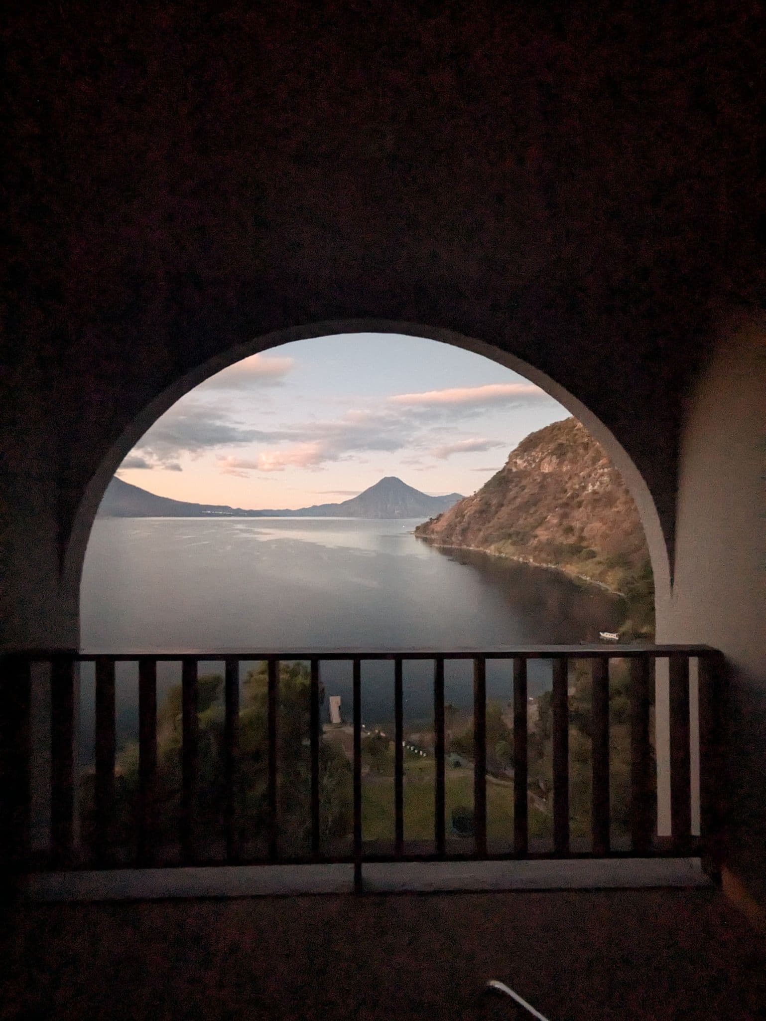 Lake Atitlán framed by an arched hotel balcony, with a volcano across the water at dusk, Guatemala.