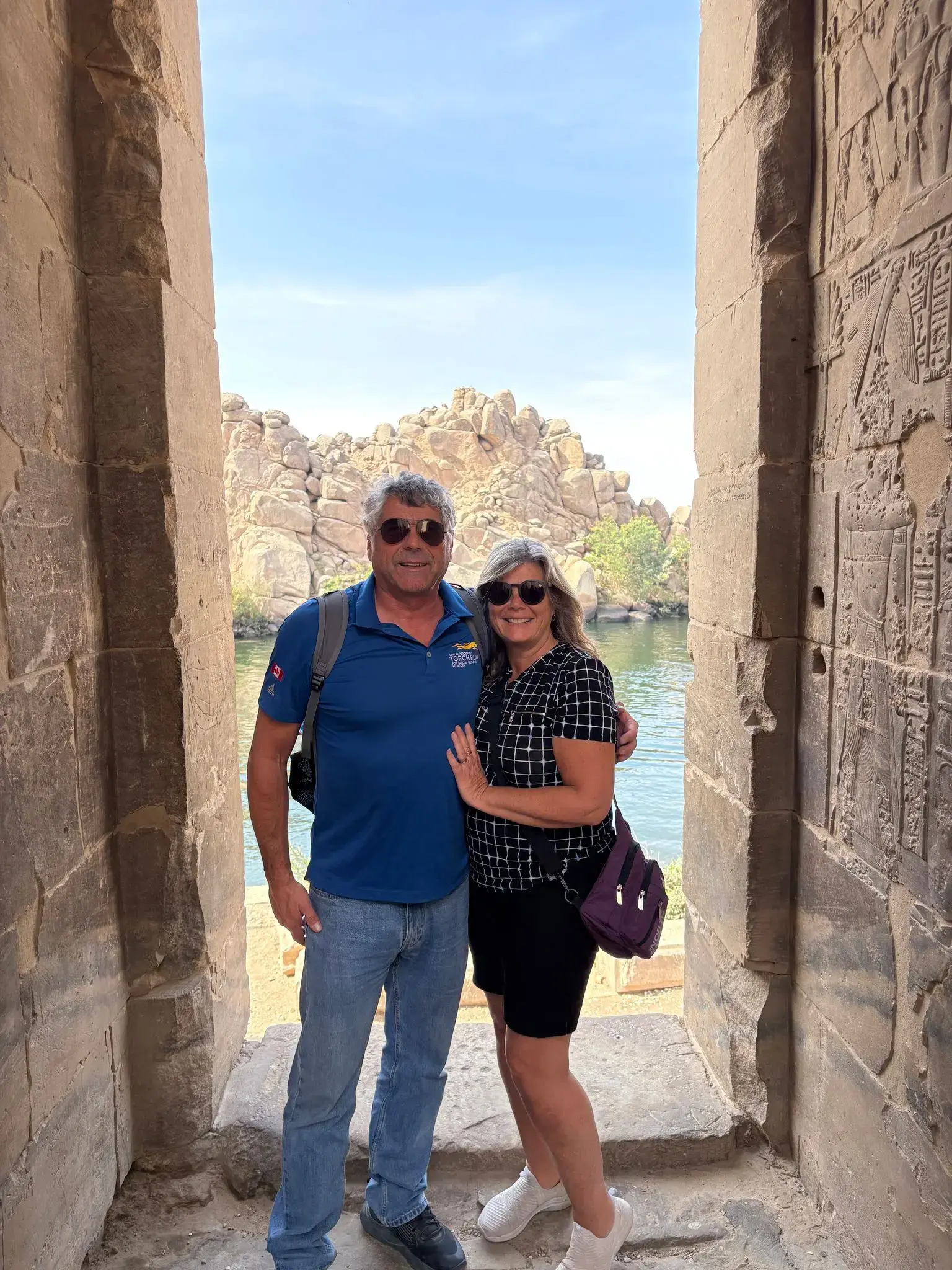 Philae Temple stone doorway with carved hieroglyphs framing a couple posing by the Nile on Agilkia Island, Aswan, Egypt.