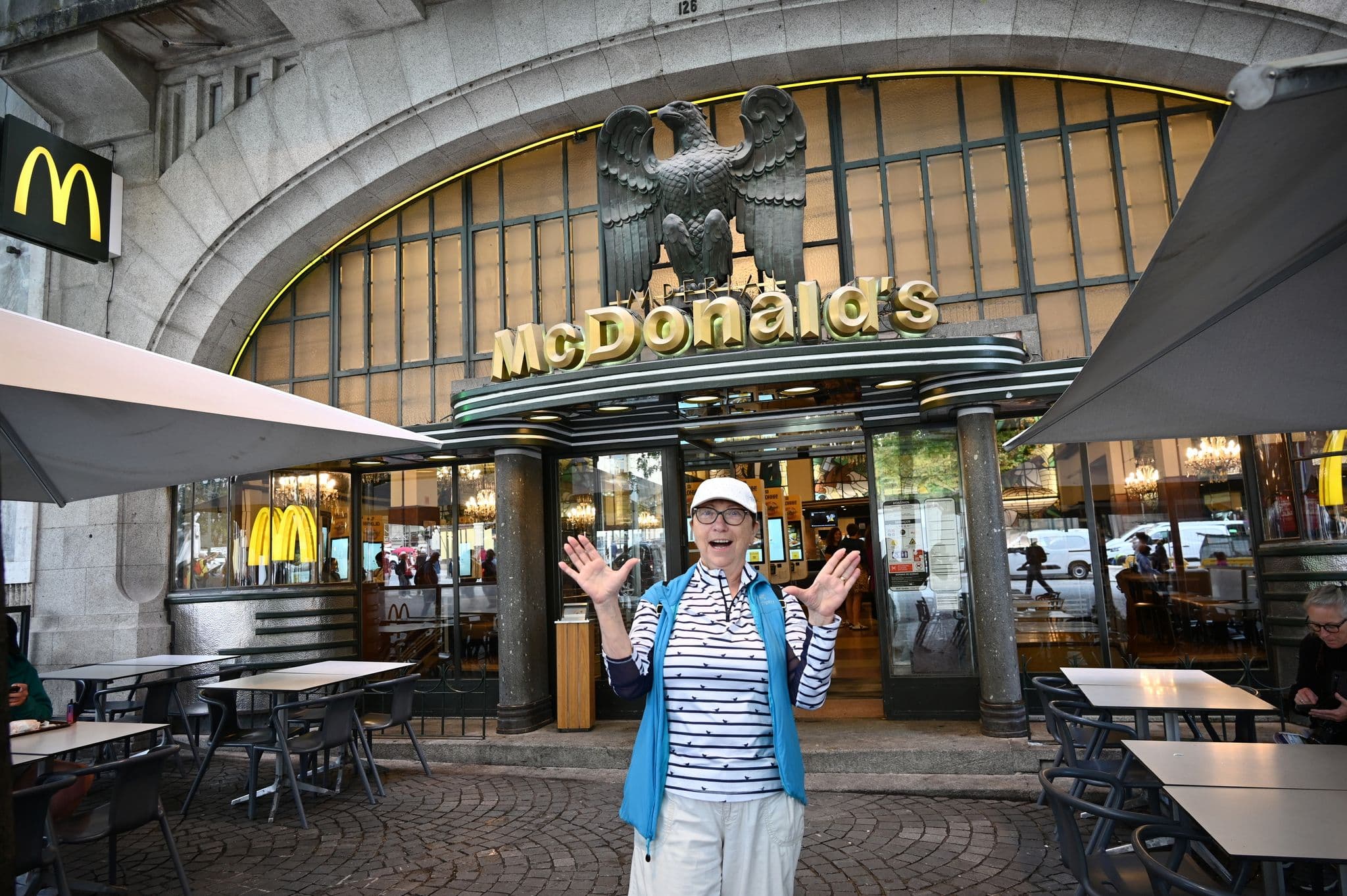 McDonald's entrance with a large eagle sculpture and a traveler posing with hands raised outside, Porto, Portugal.