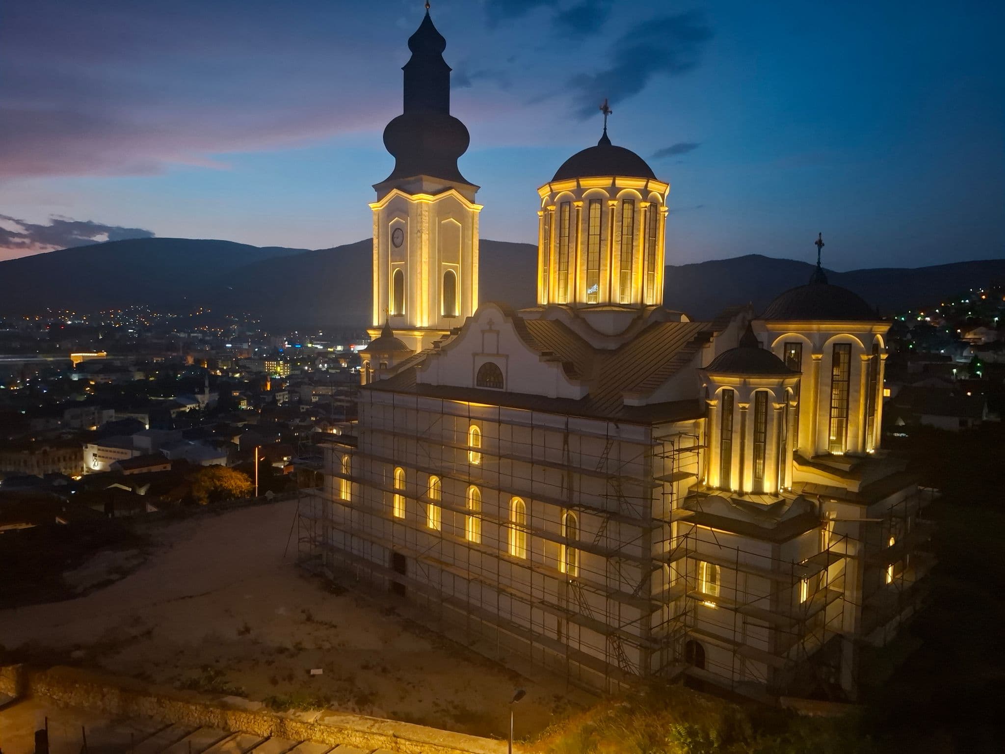 Illuminated Orthodox church under renovation in Mostar, Bosnia and Herzegovina, seen from a hotel balcony at dusk over the city.