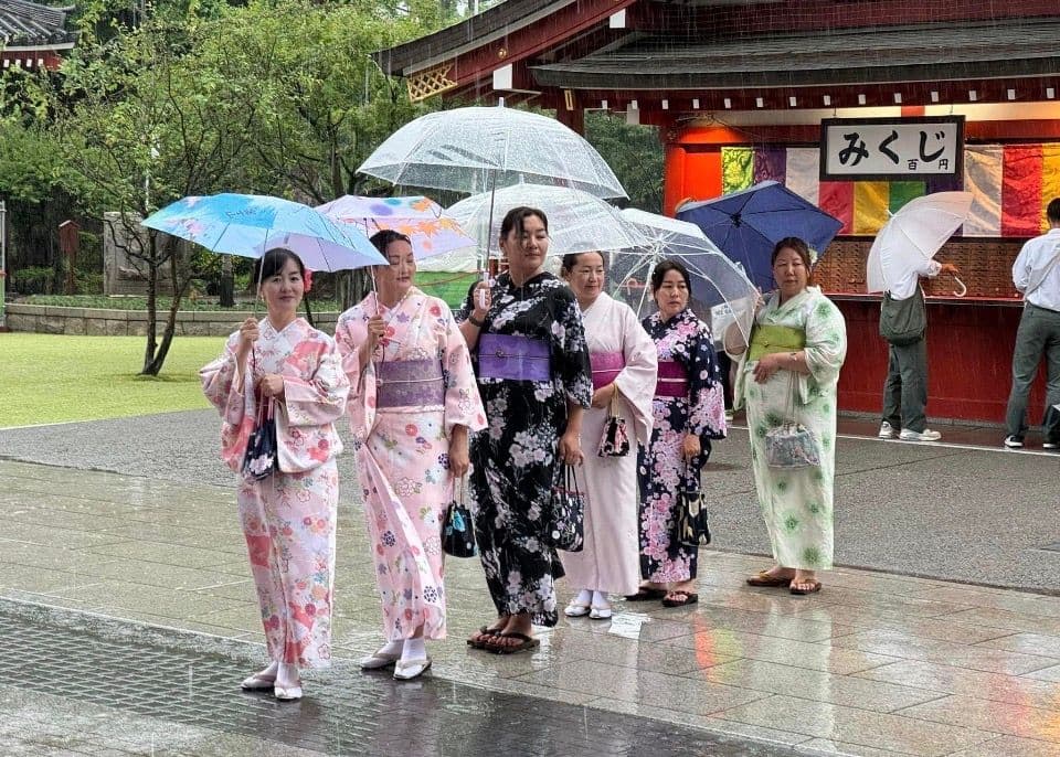Group of women in colorful kimonos holding umbrellas outside an omikuji stall at a shrine in Tokyo, Japan