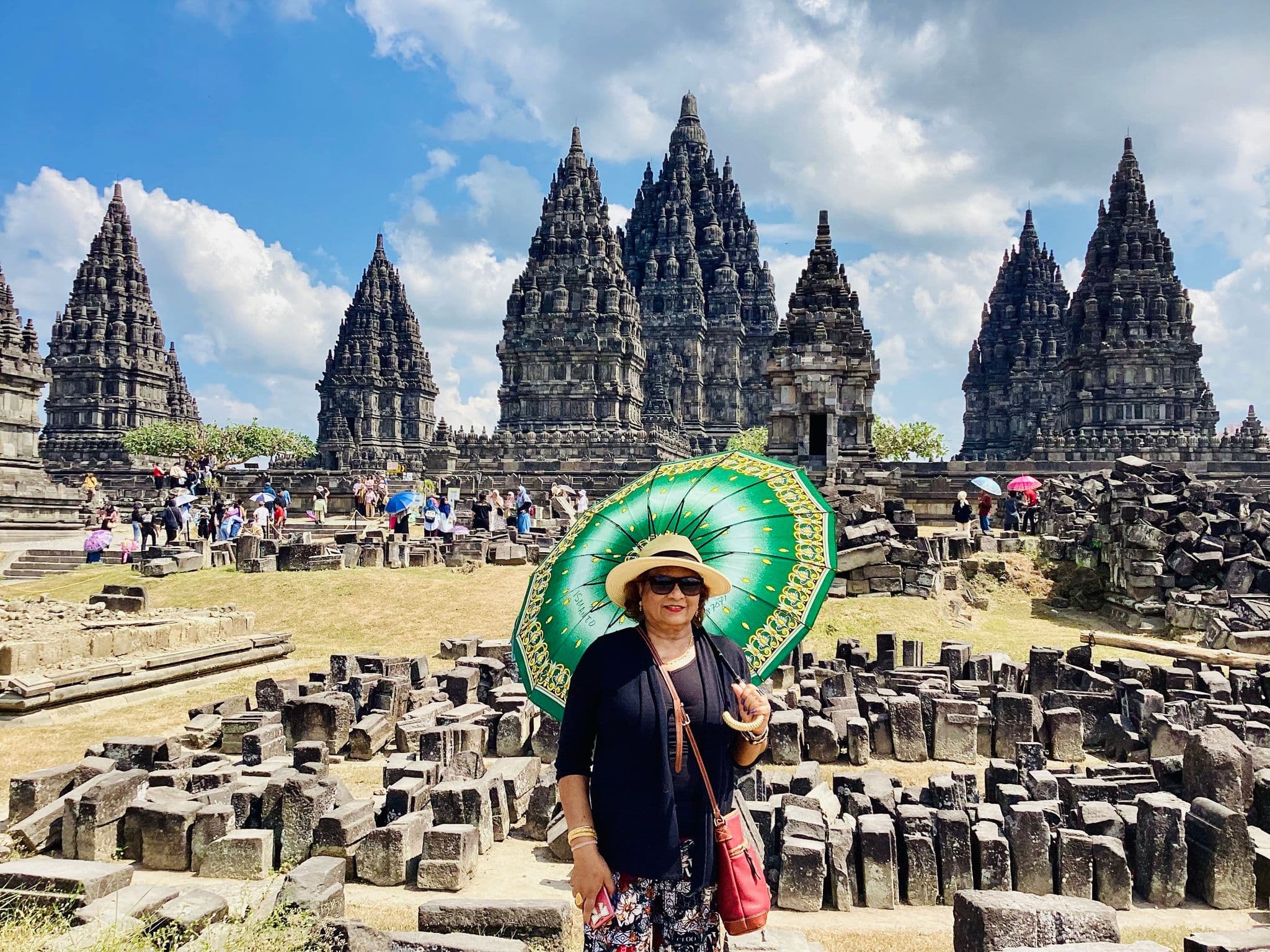 Prambanan Temple complex with a traveler holding a green umbrella in the foreground, Yogyakarta, Indonesia.