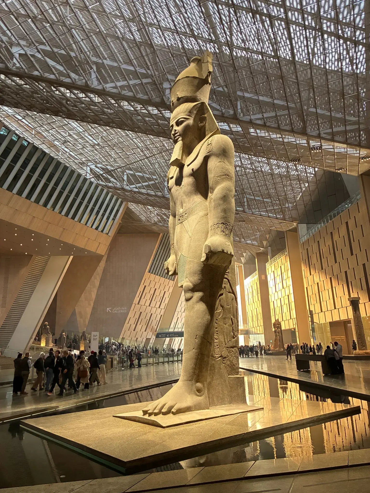 Standing pharaoh statue inside the Grand Egyptian Museum in Giza, Egypt, with visitors walking through the gallery