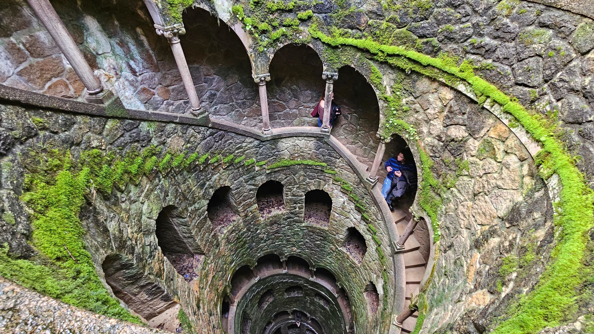 Initiation Well at Quinta da Regaleira, Sintra, Portugal, spiral stone staircase descending with a person on the walkway.