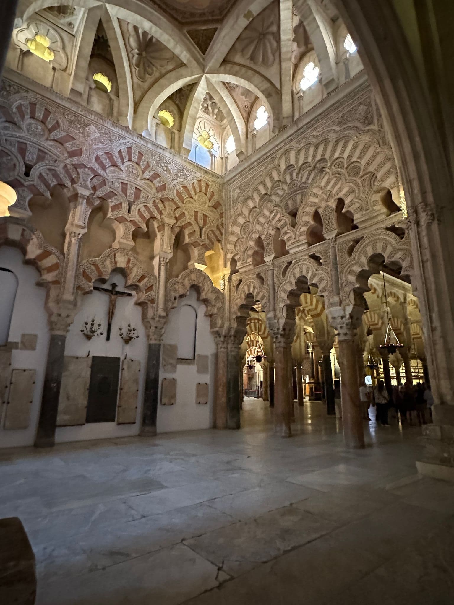 Interior of the Mosque–Cathedral of Córdoba showing red-and-white horseshoe arches and a vaulted ceiling, with visitors in the background, Córdoba, Spain.