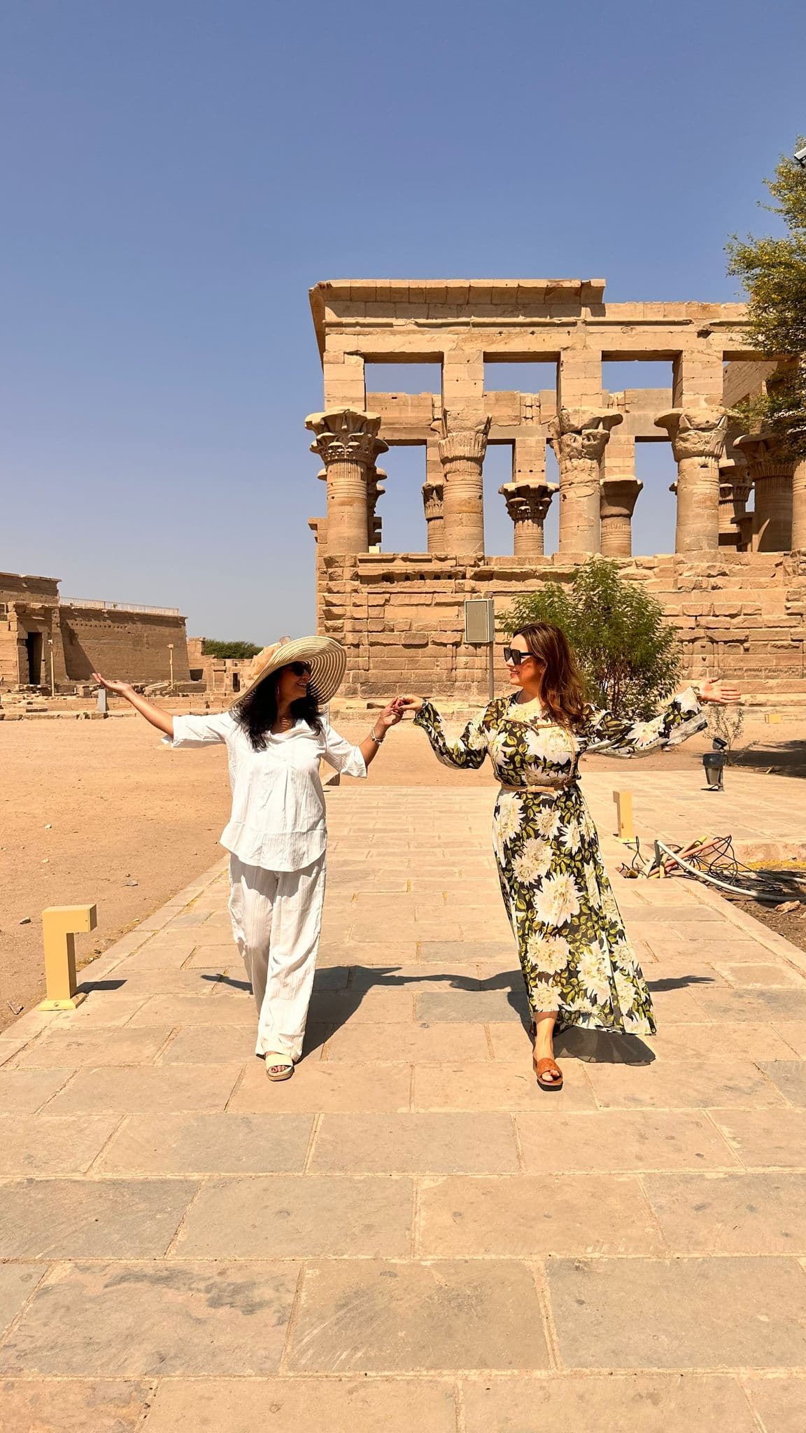 Temple of Philae columns on Agilkia Island with two women holding hands walking on a stone path, Egypt.