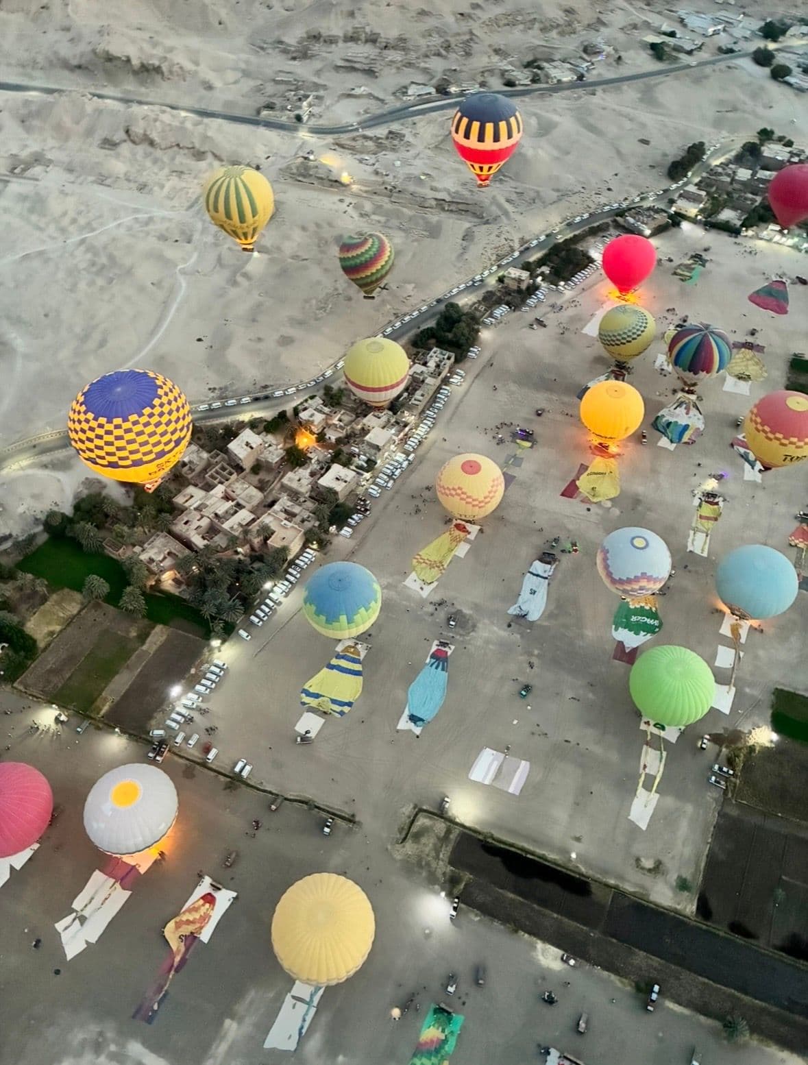 Hot air balloons floating above the Valley of the Queens near Luxor, Egypt, over desert and a small village.