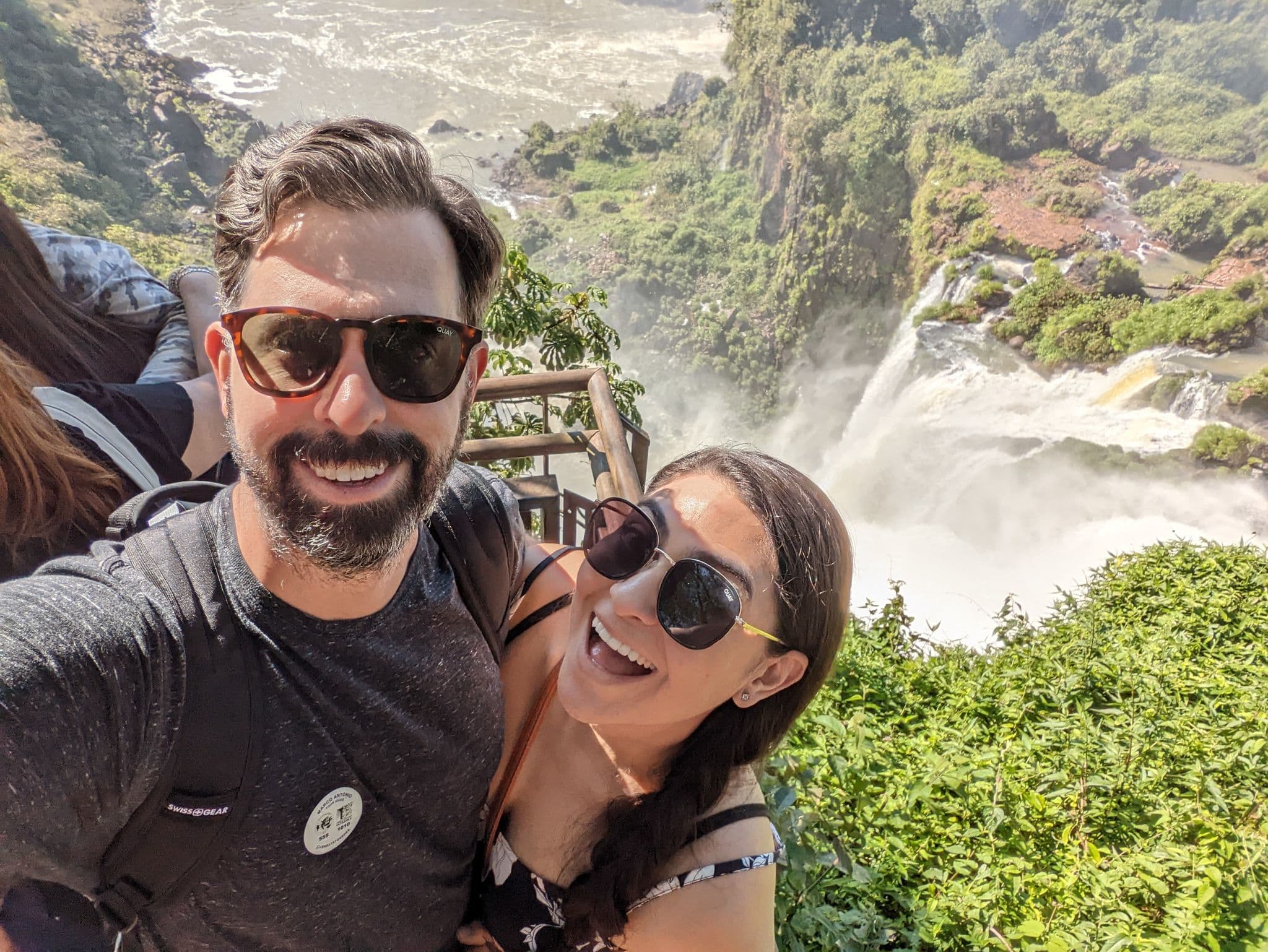 Iguazu Falls cascading over rocky cliffs with a smiling couple taking a selfie on a viewing platform