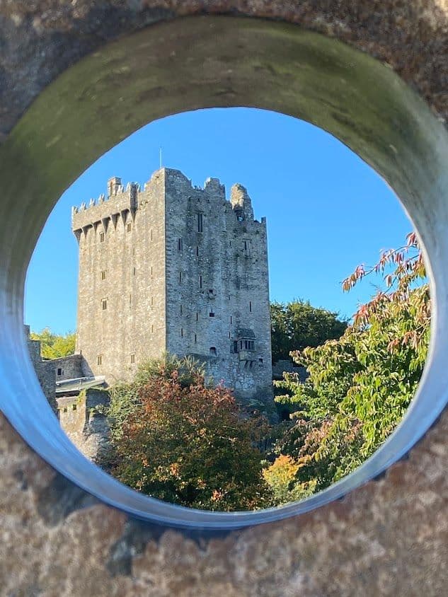 Blarney Castle tower framed through a circular stone opening with autumn trees and a blue sky, Blarney, Ireland