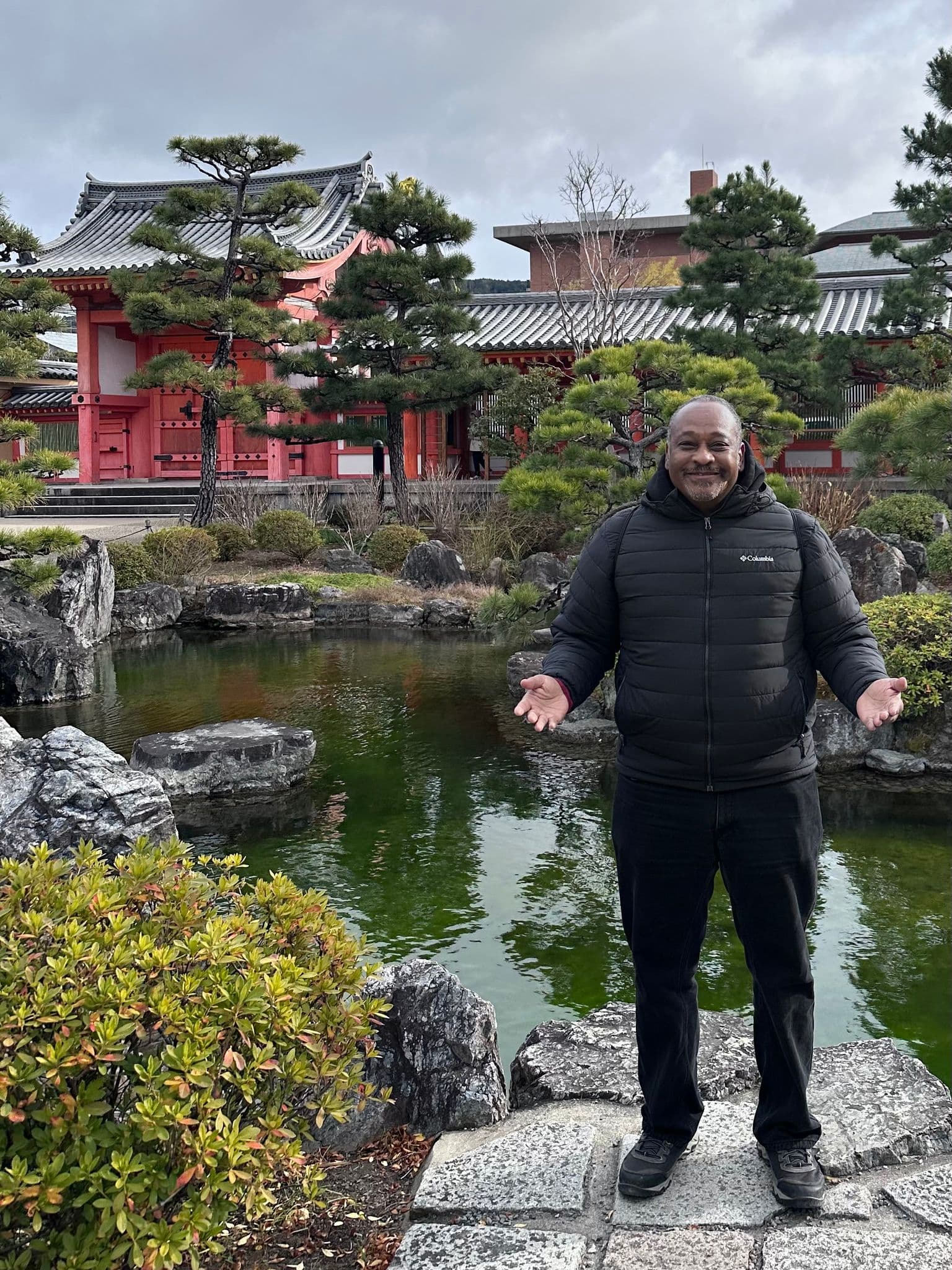 Sanjusangen-do temple and garden pond in Kyoto with a traveler standing on stones near the water.