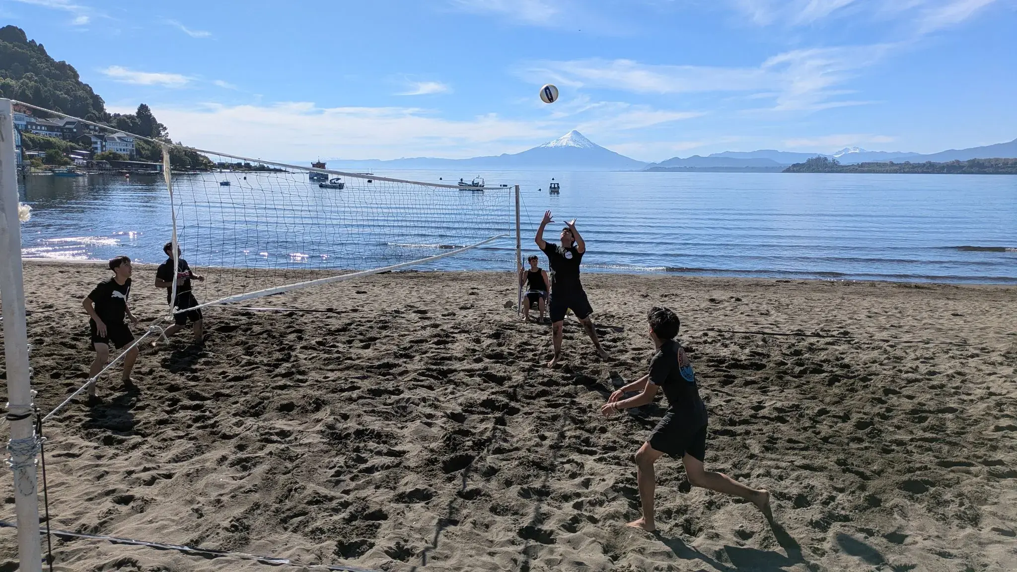Volcán Osorno rising above Lake Llanquihue with players hitting a volleyball on the sandy shore in Puerto Varas, Chile.