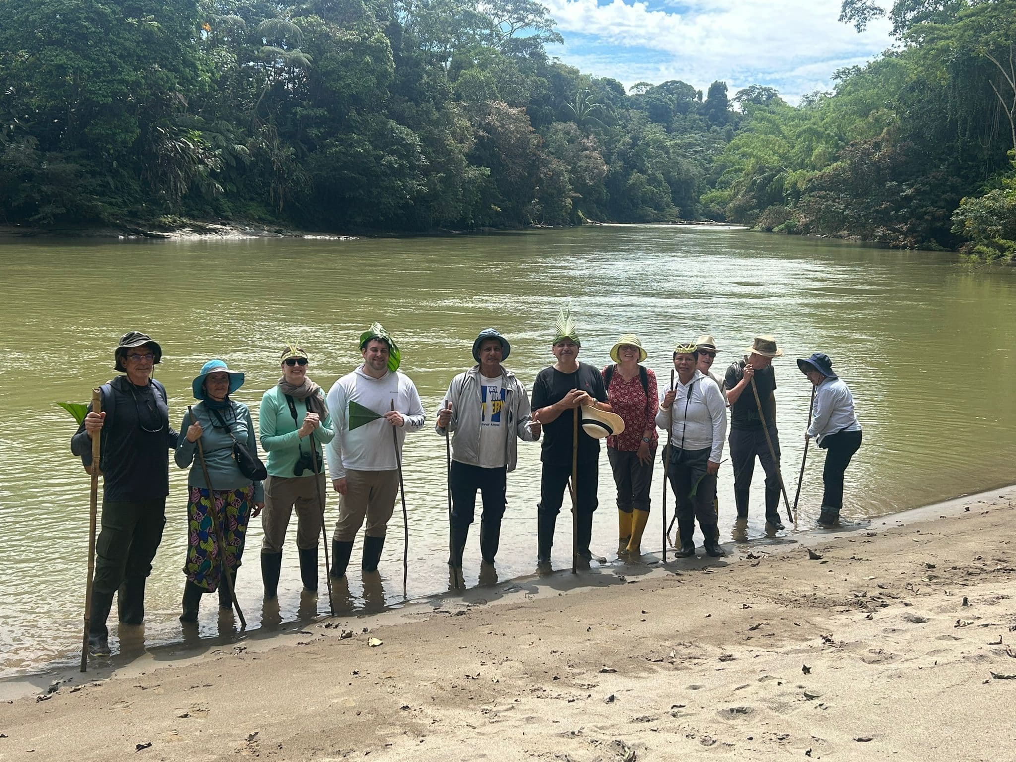 A line of travelers standing in shallow water on a riverbank in the Amazon rainforest, Ecuador, during a guided trip.