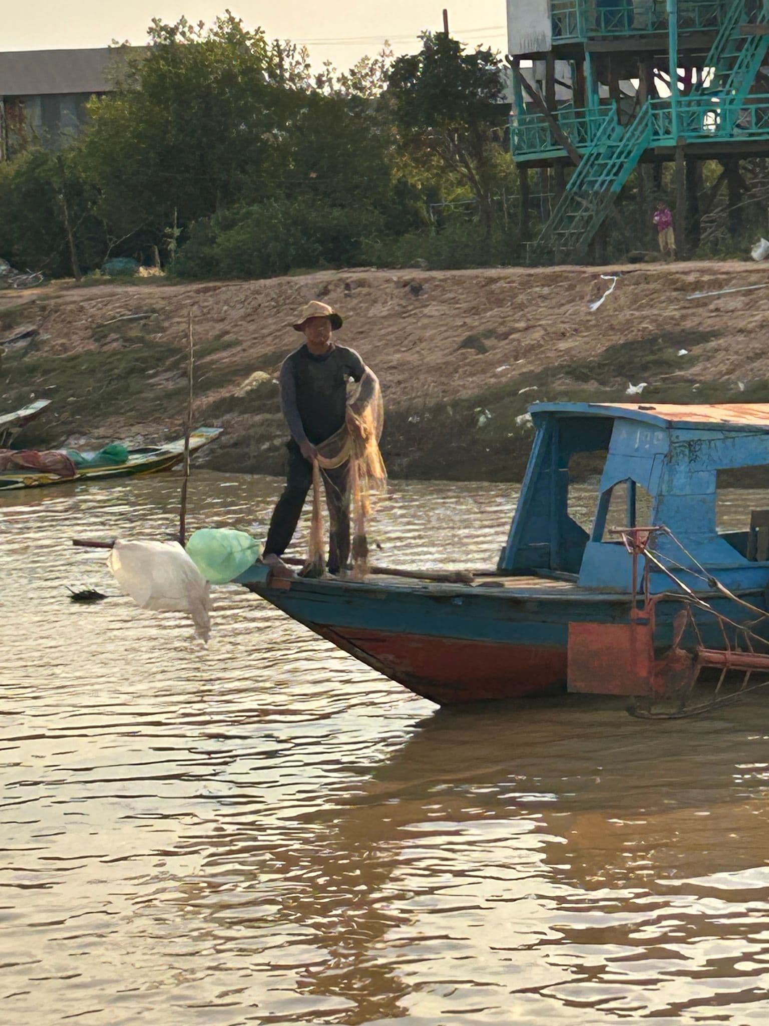 Fisherman standing on a wooden boat casting a net on Tonle Sap Lake at Kampong Phluk, Cambodia.