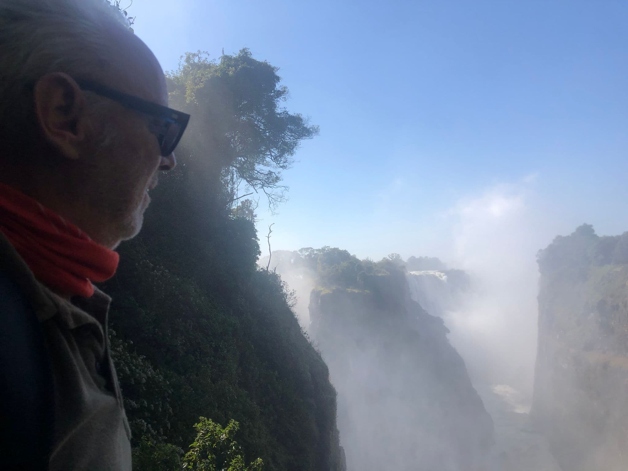 Victoria Falls with mist-filled gorge and a traveler in profile looking out, Victoria Falls, Zimbabwe.