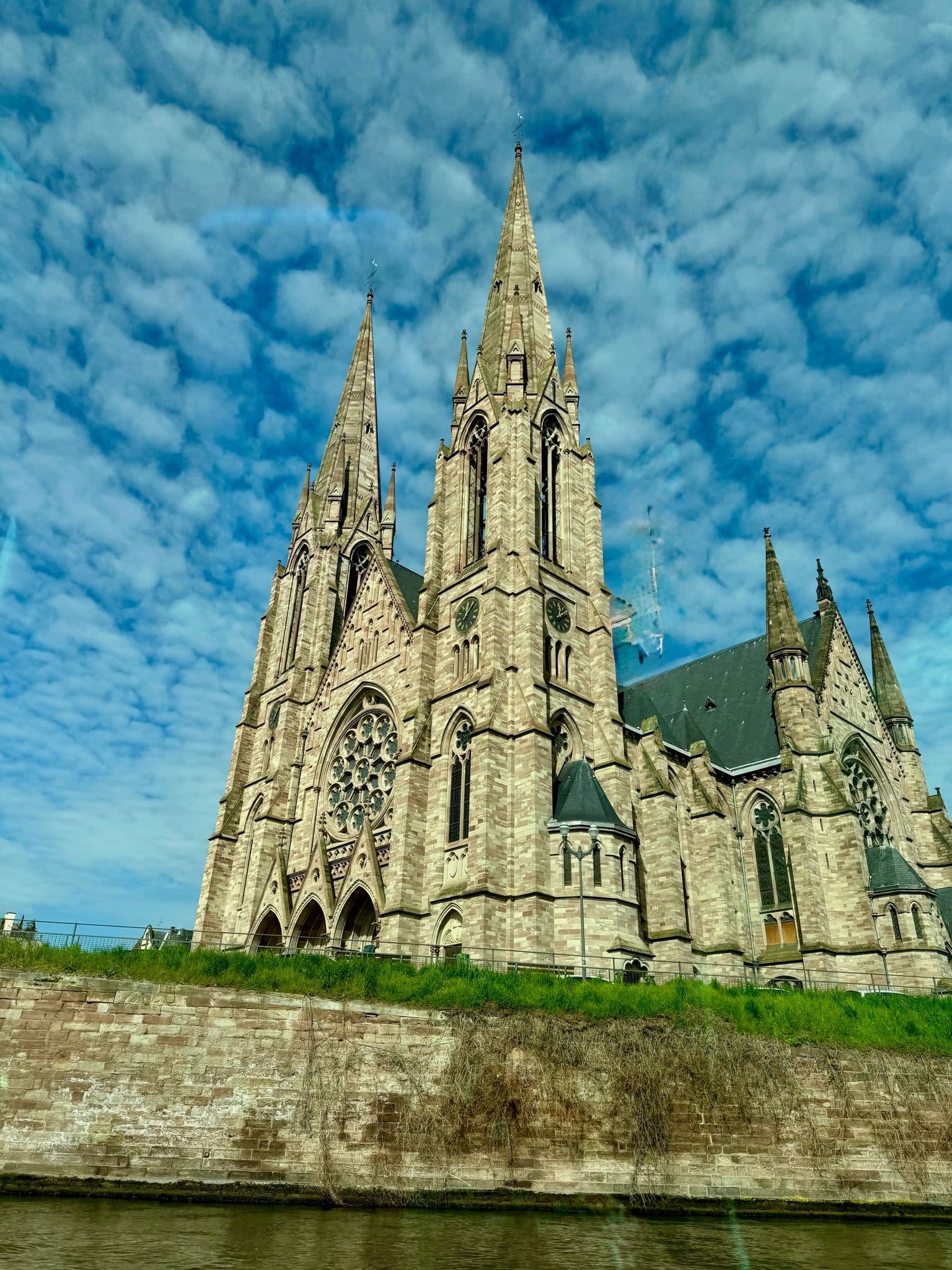 Saint Paul's Church (Église Saint-Paul) in Strasbourg, France, seen from the riverside with its twin spires against a cloud-filled sky.