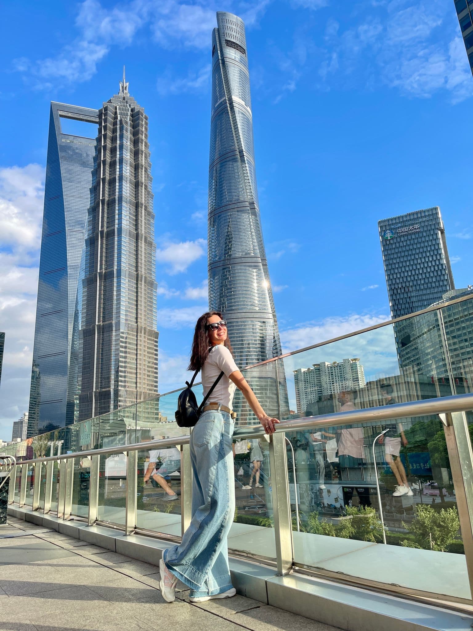 Shanghai Tower and the Shanghai World Financial Center with a traveler leaning on a glass railing on a Lujiazui pedestrian bridge, Shanghai, China.