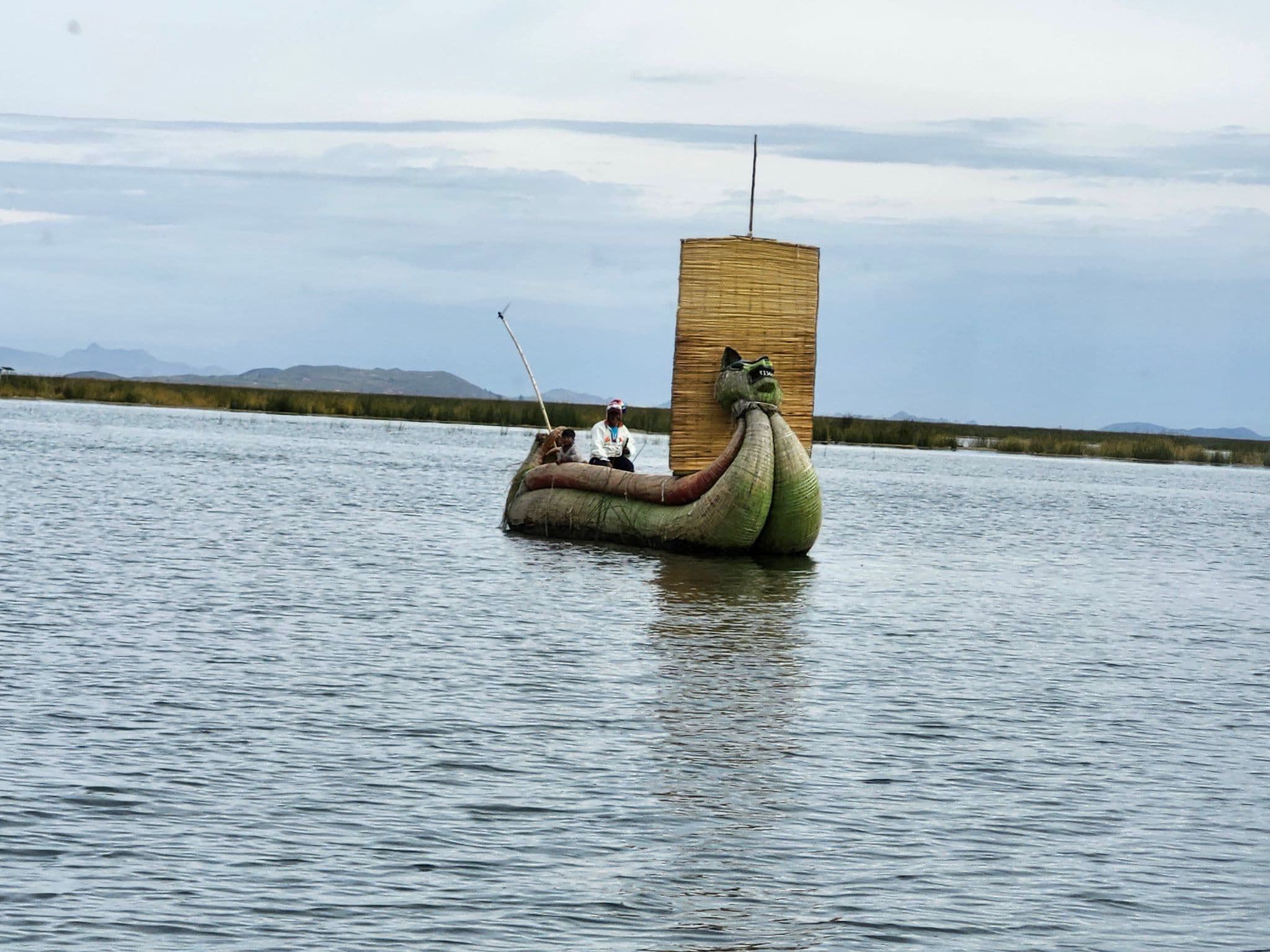 Reed boat shaped like an animal with two people aboard sailing on Lake Titicaca.