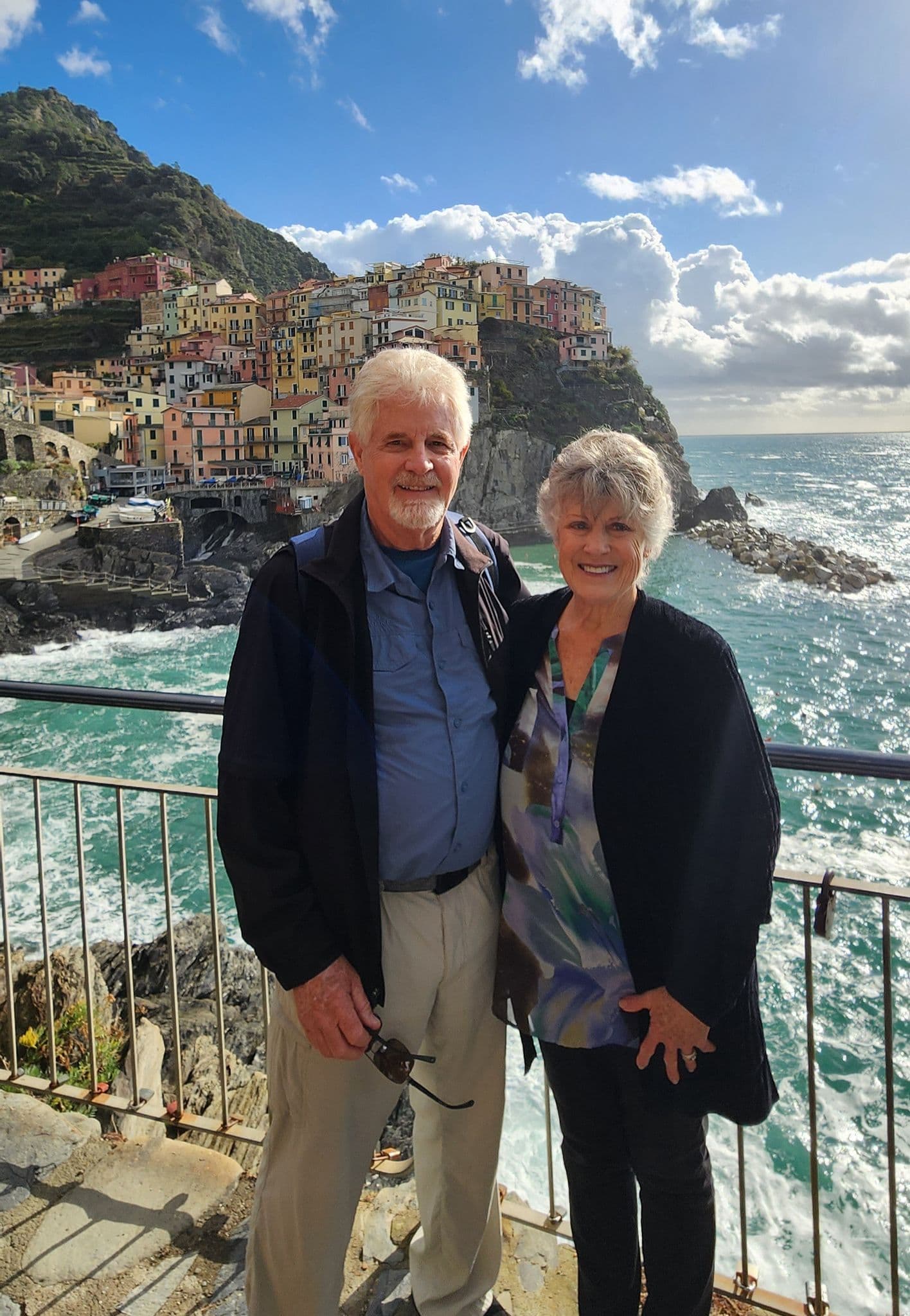 Colorful cliffside village of Cinque Terre with a couple posing at a railing overlooking the sea, Cinque Terre, Italy.
