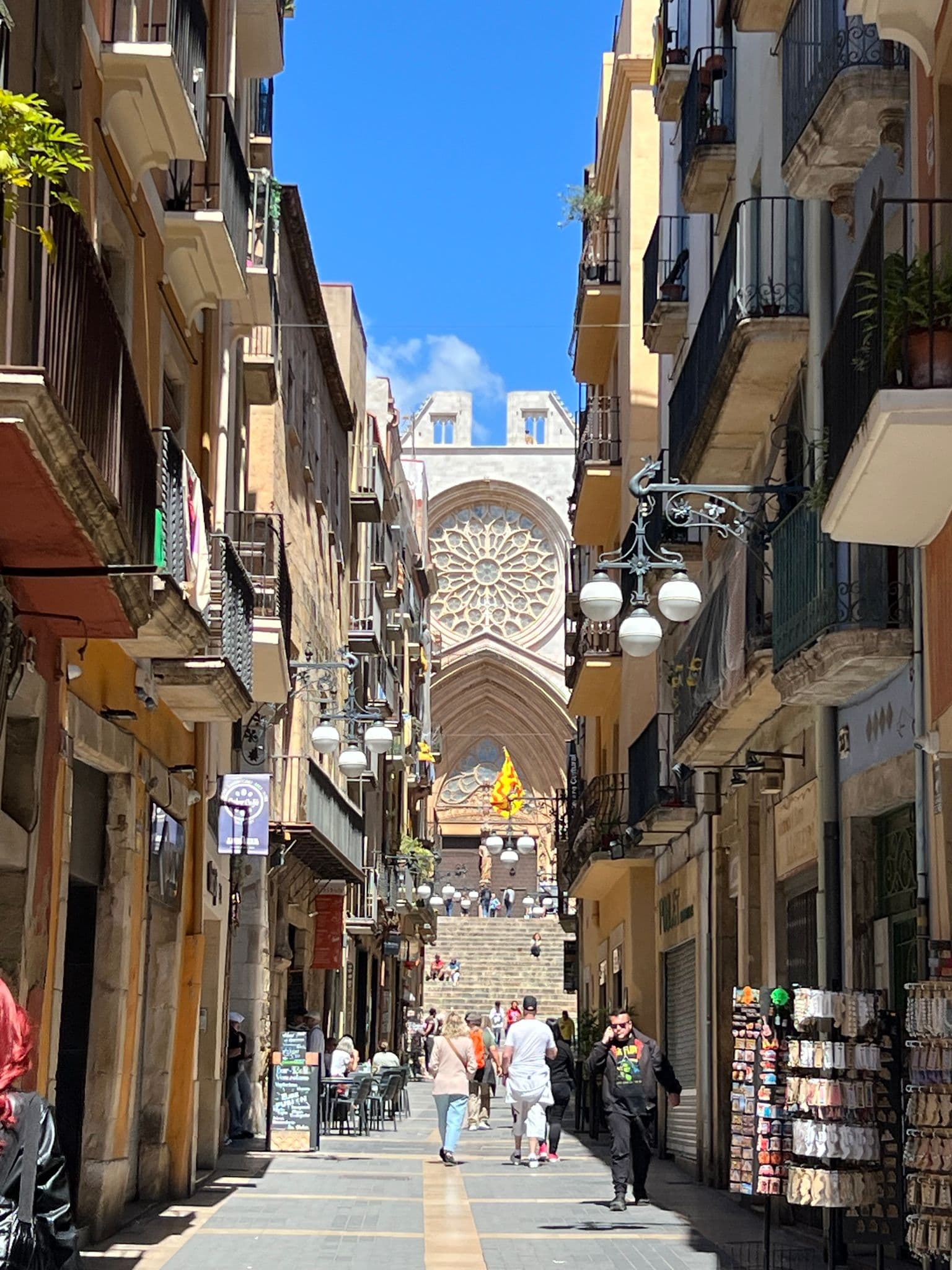 Rose window and steps of Tarragona Cathedral (Cathedral of Santa Tecla) seen down a narrow street with people walking, Tarragona, Spain.