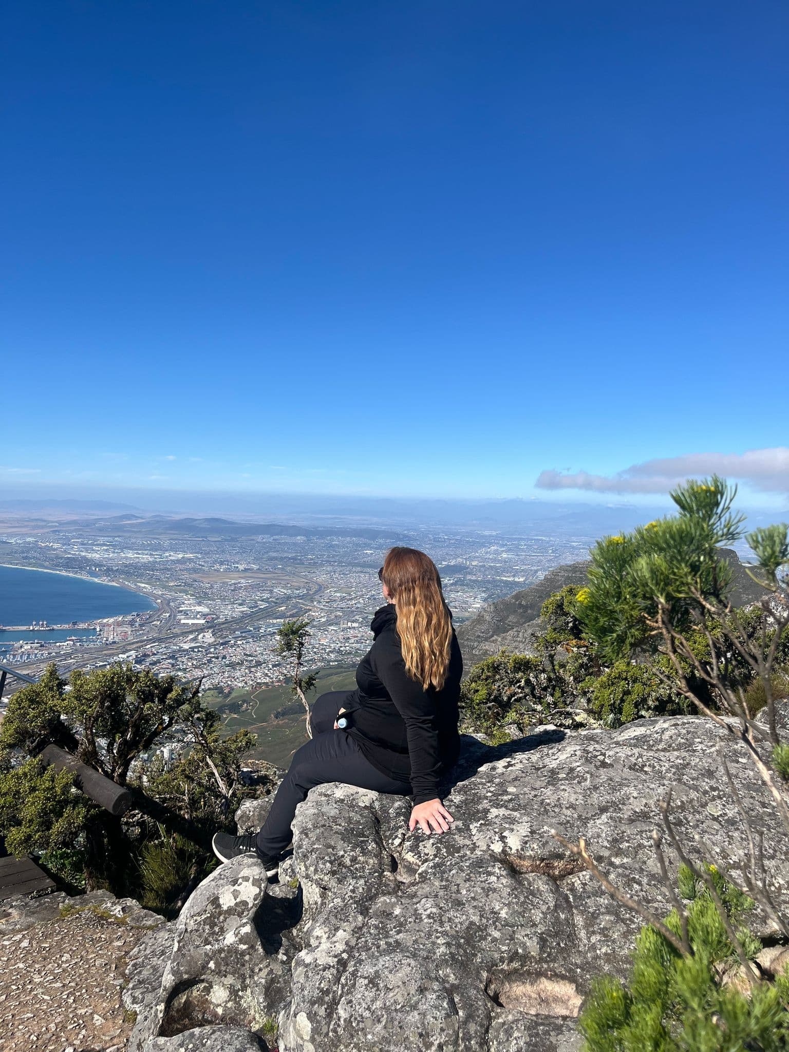 View from Table Mountain overlooking Cape Town and the Atlantic coast, with a traveler seated on a rocky ledge