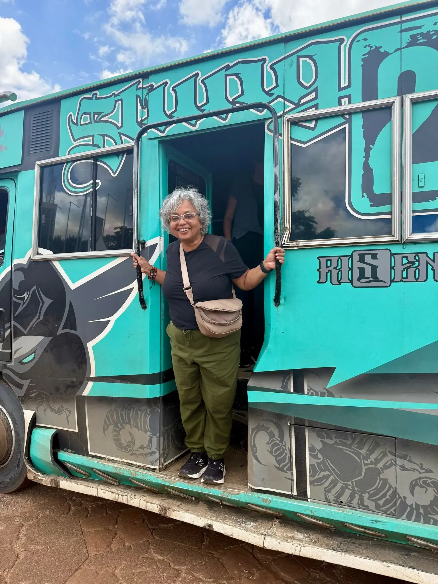 Turquoise matatu with a woman stepping out of the doorway onto a dusty street in Nairobi, Kenya.