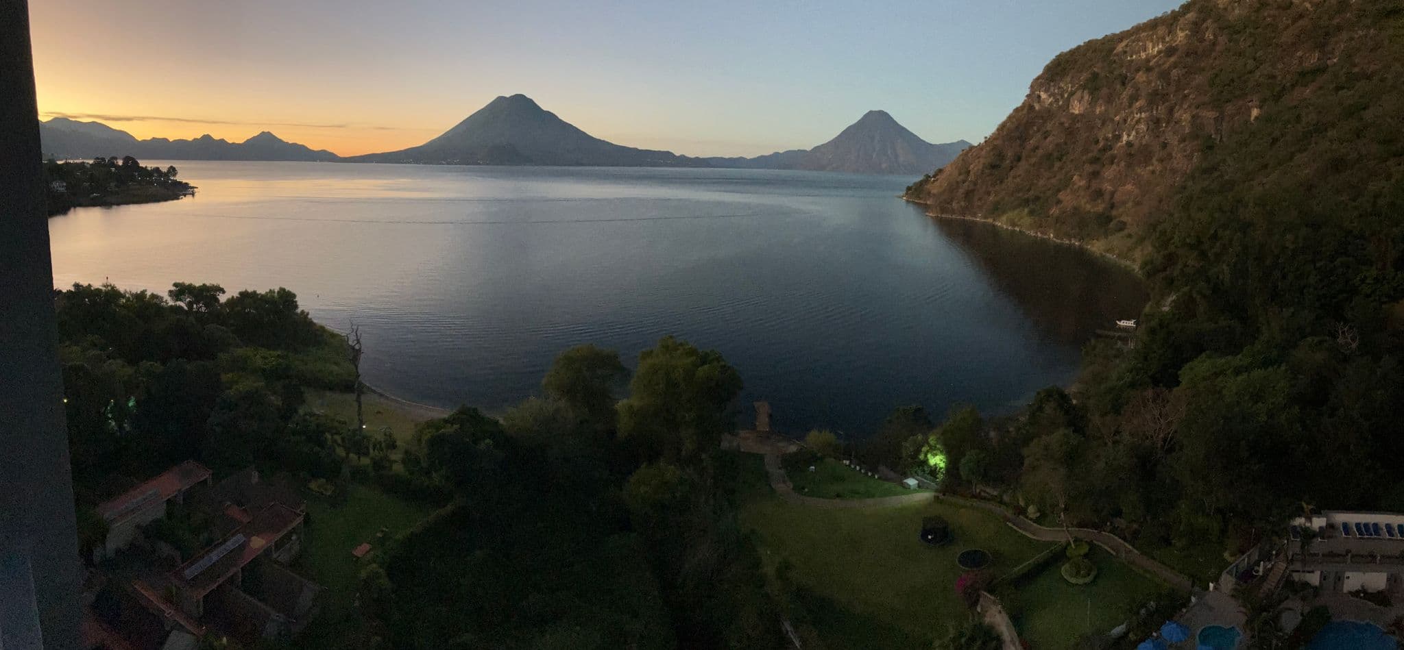 Lake Atitlán with volcanoes rising across the water at sunrise, seen from a lakeside hillside, Guatemala.