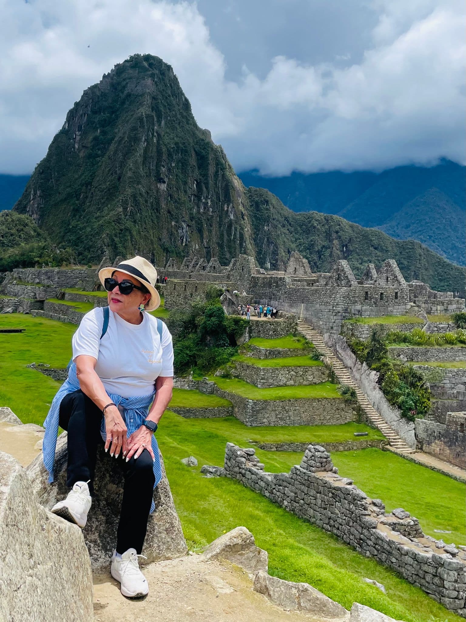Machu Picchu ruins with Huayna Picchu behind and a traveler sitting on a stone ledge, Cusco Region, Peru