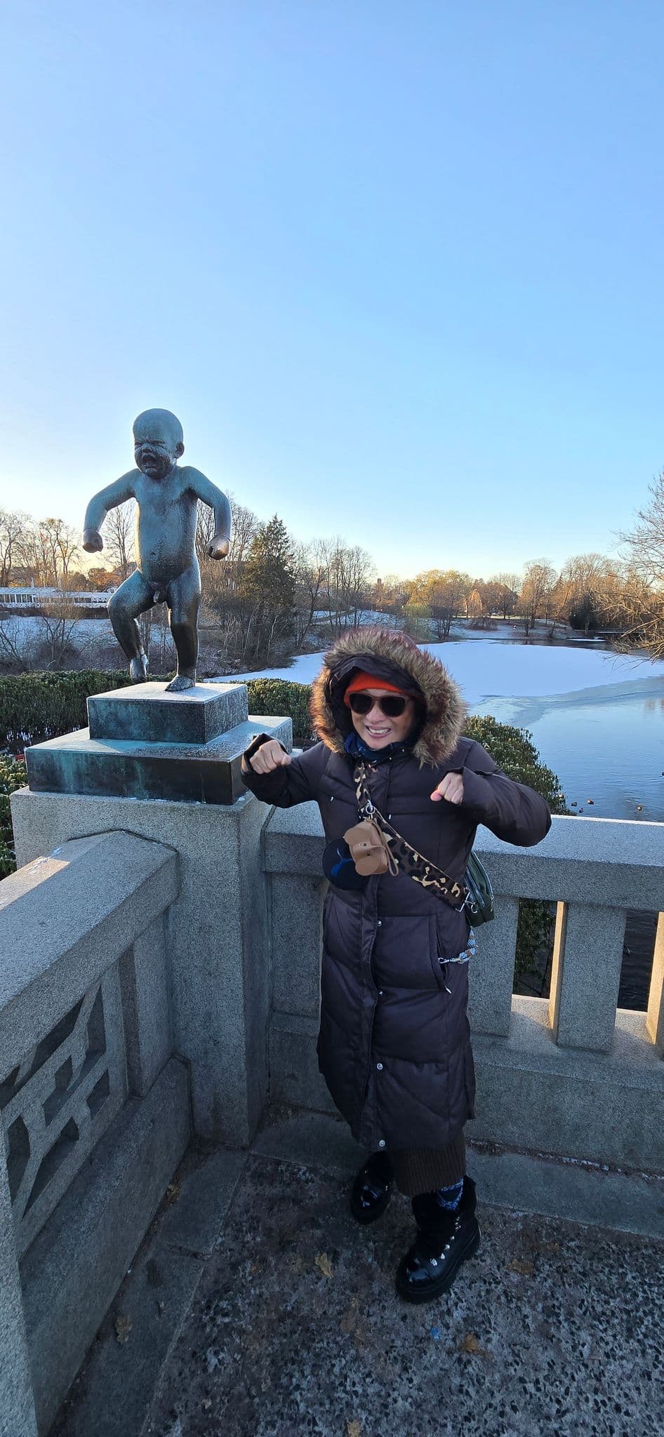 Sinnataggen (Angry Boy) sculpture on a bridge, with a woman mimicking its stamping pose at Vigeland Park, Oslo, Norway