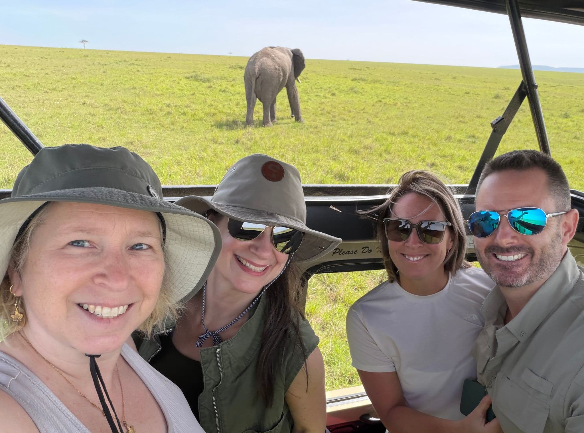 Elephant on the Maasai Mara grasslands with four travelers smiling in a safari vehicle selfie, Maasai Mara National Reserve, Kenya.