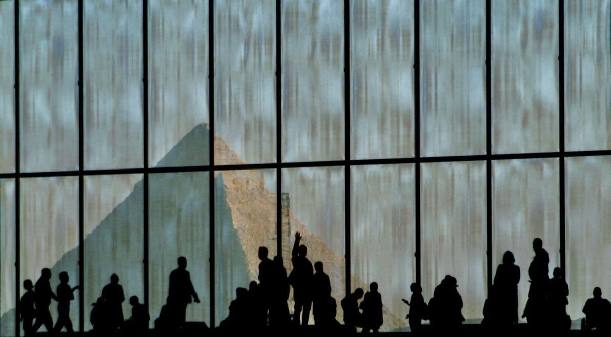 Great Pyramid of Giza framed through the Grand Egyptian Museum's tall windows with silhouetted visitors inside, Egypt.