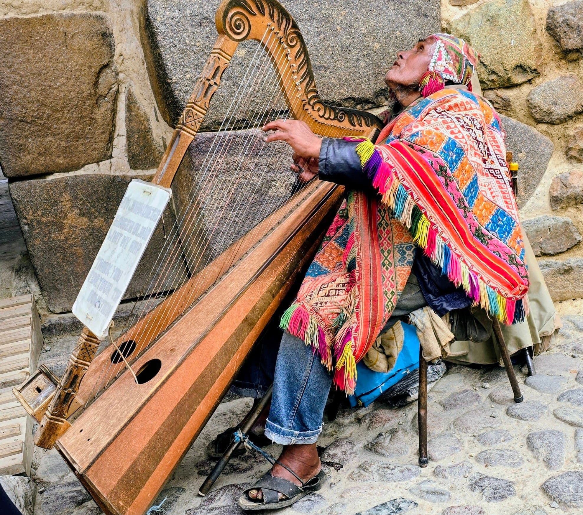 Musician playing a wooden Andean harp against Inca stone walls in Ollantaytambo, Peru.