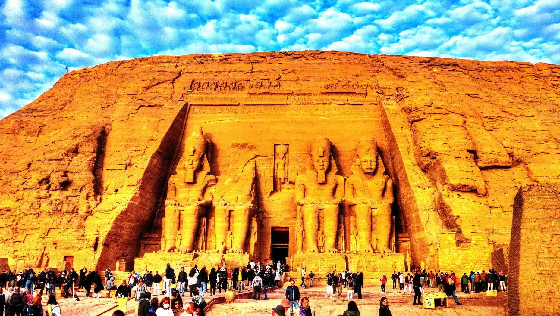 Colossal seated statues at Abu Simbel's Great Temple with tourists gathered in front, Aswan region, Egypt.