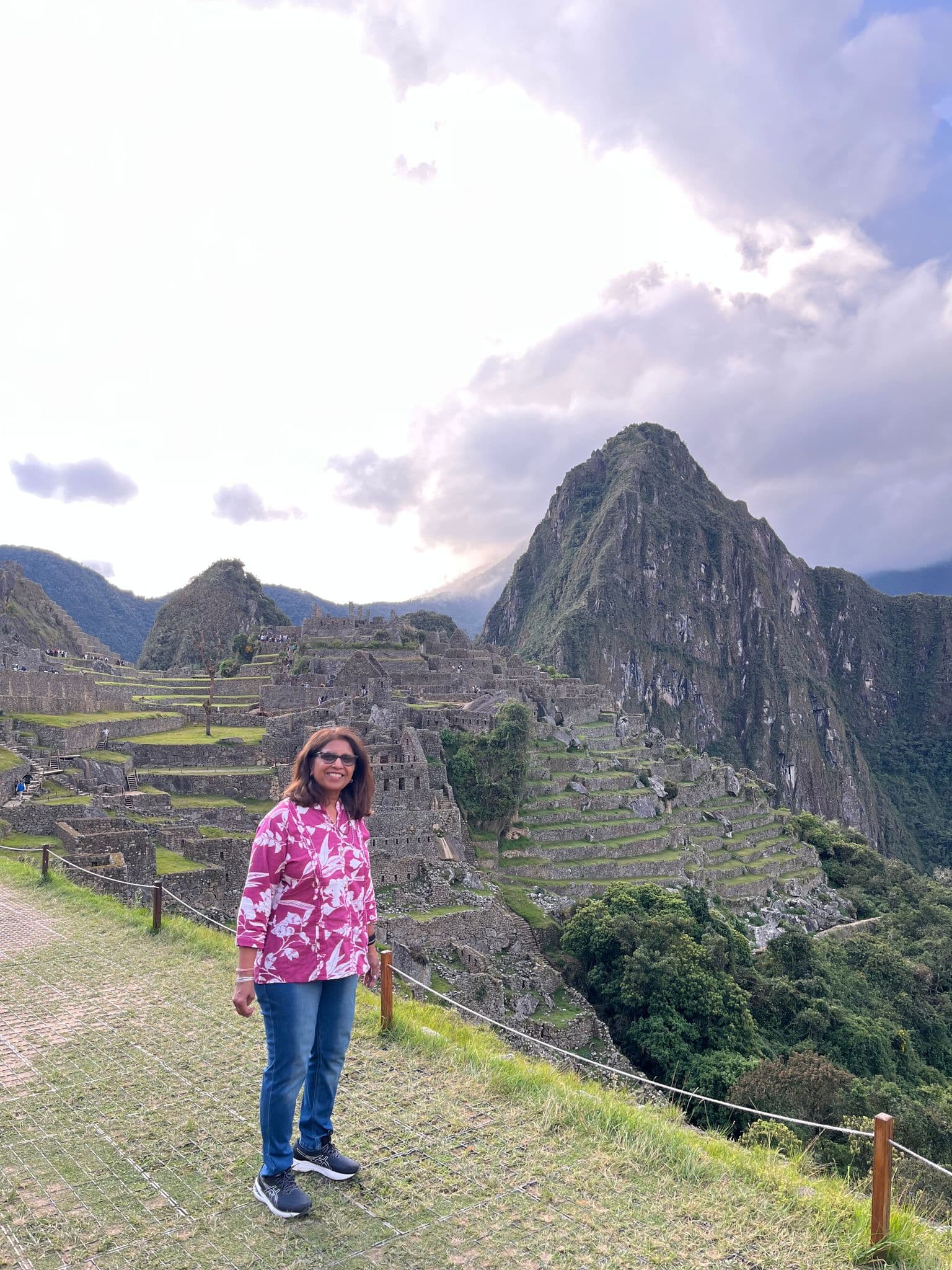 Machu Picchu ruins and Huayna Picchu in the background, a traveler standing on a grassy terrace during a tour in Cusco, Peru.