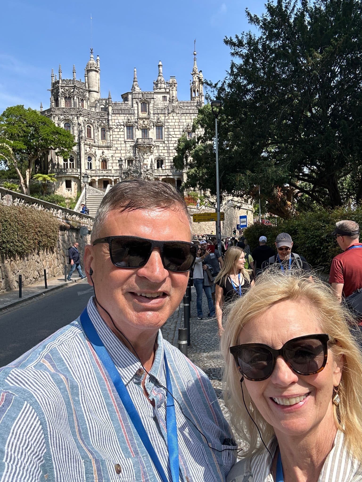 Regaleira Palace in Sintra, Portugal with two travelers smiling for a selfie on a crowded walking tour near the castle.